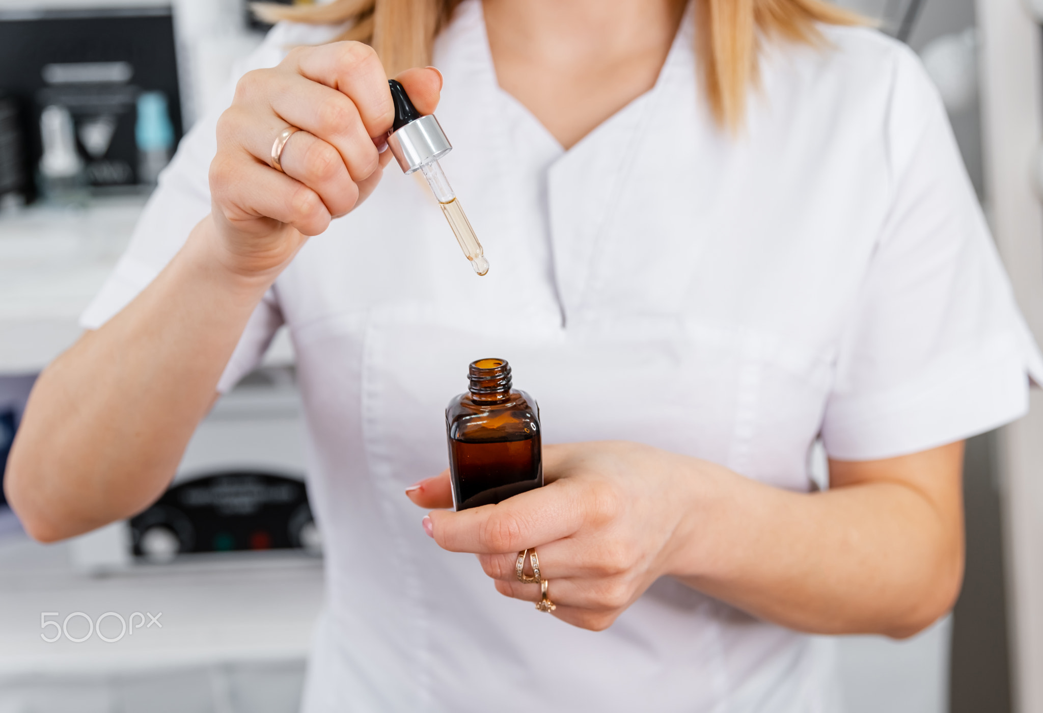 The beautician is putting essential oil on the face of women.