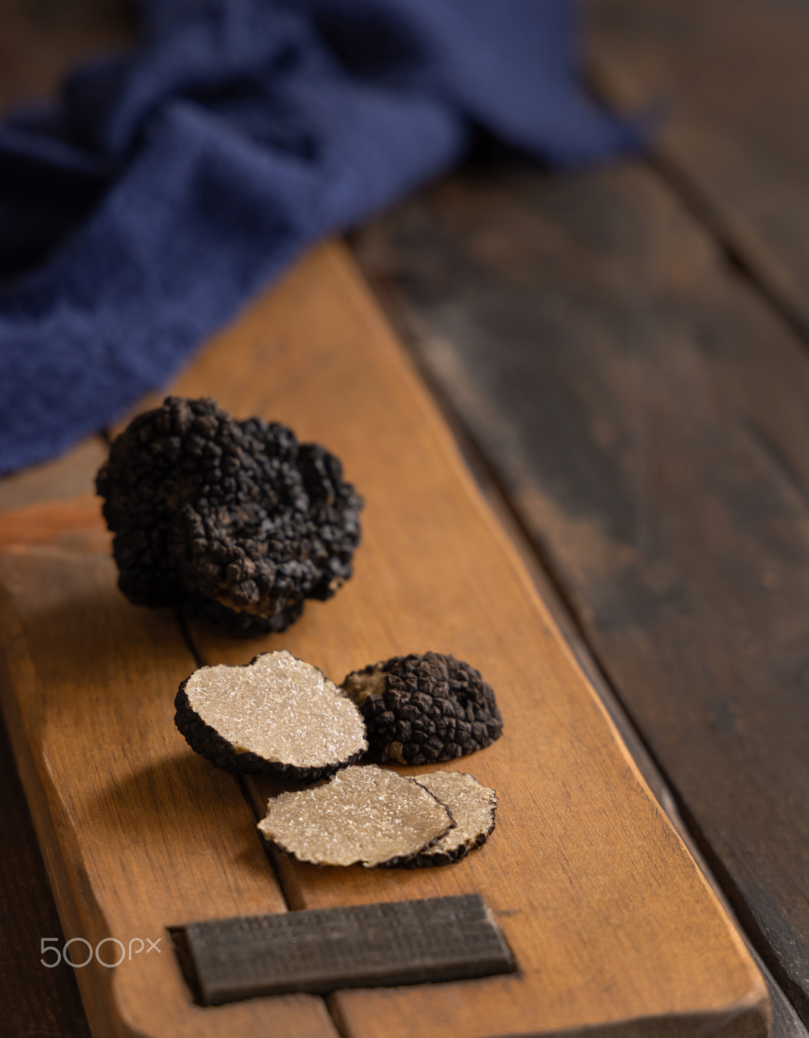 Whole and sliced black truffles mushroom on wooden board on dark brown table, close up