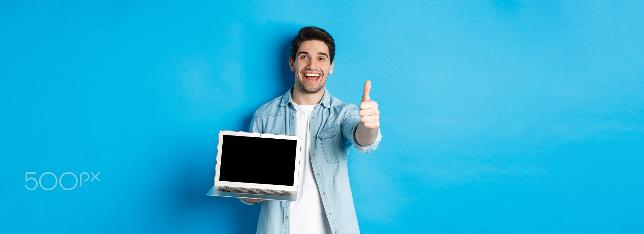 Image of satisfied handsome man showing laptop screen, thumbs-up in