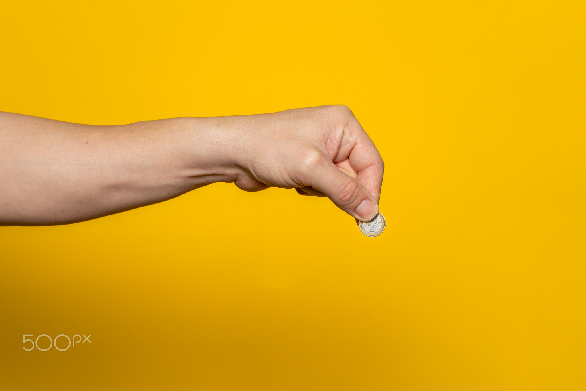 Strong man's hand ready to drop a coin isolated on a yellow background