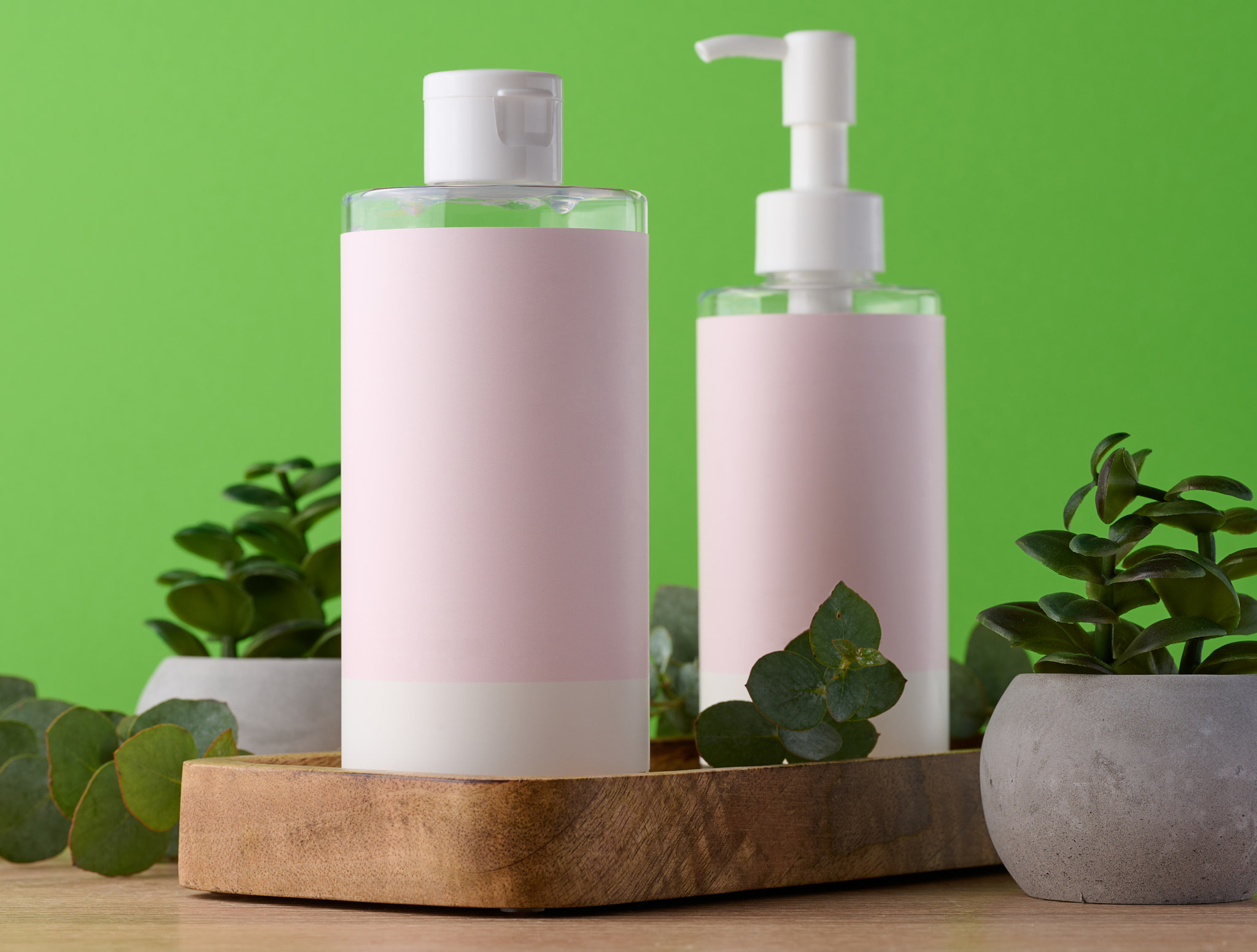 Two bottles for cosmetics with a pink paper label on a green background. Bottle for tonic, gel
