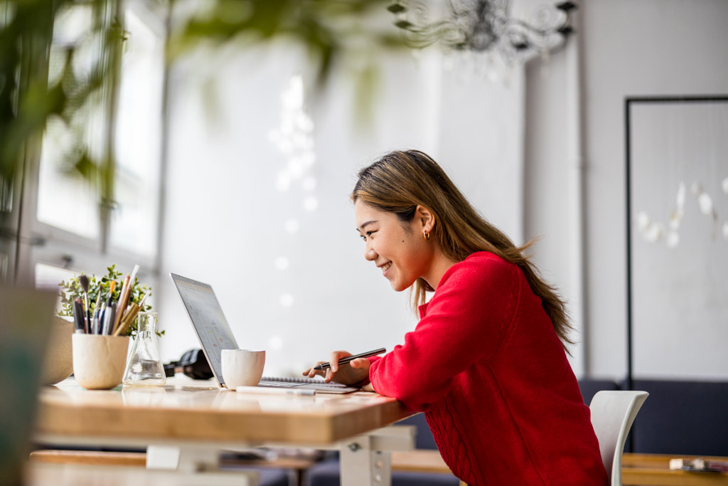 Jeune femme assise à un bureau travaillant sur un ordinateur portable par Edyta Pawlowska sur 500px.com