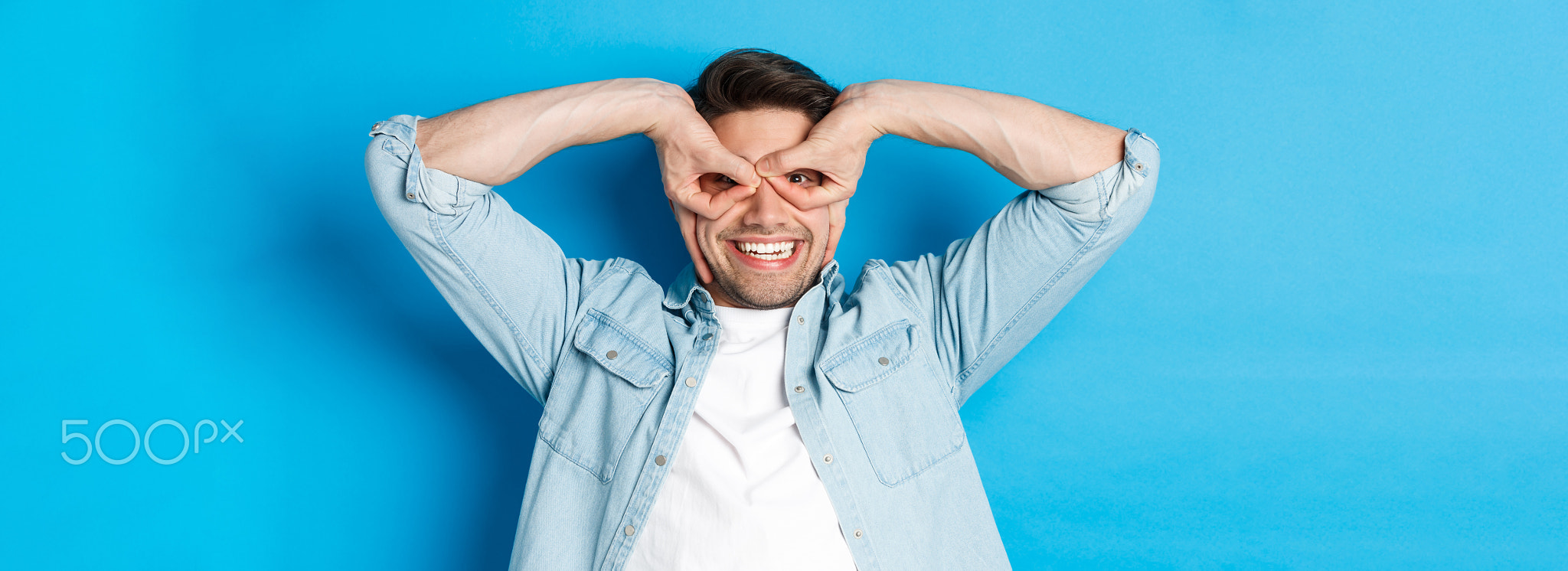 Young caucasian guy showing funny expression, making superhero mask