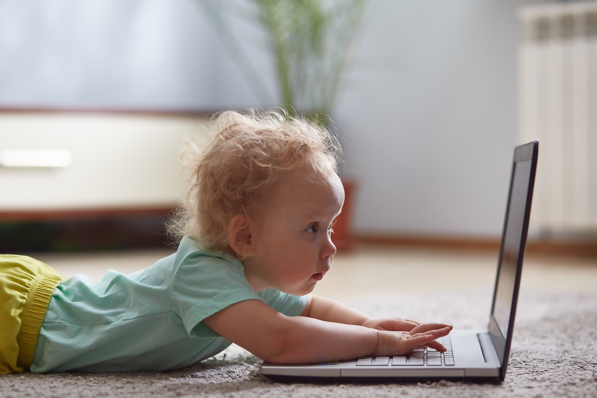 small child at a computer lying on a carpet in a living room.