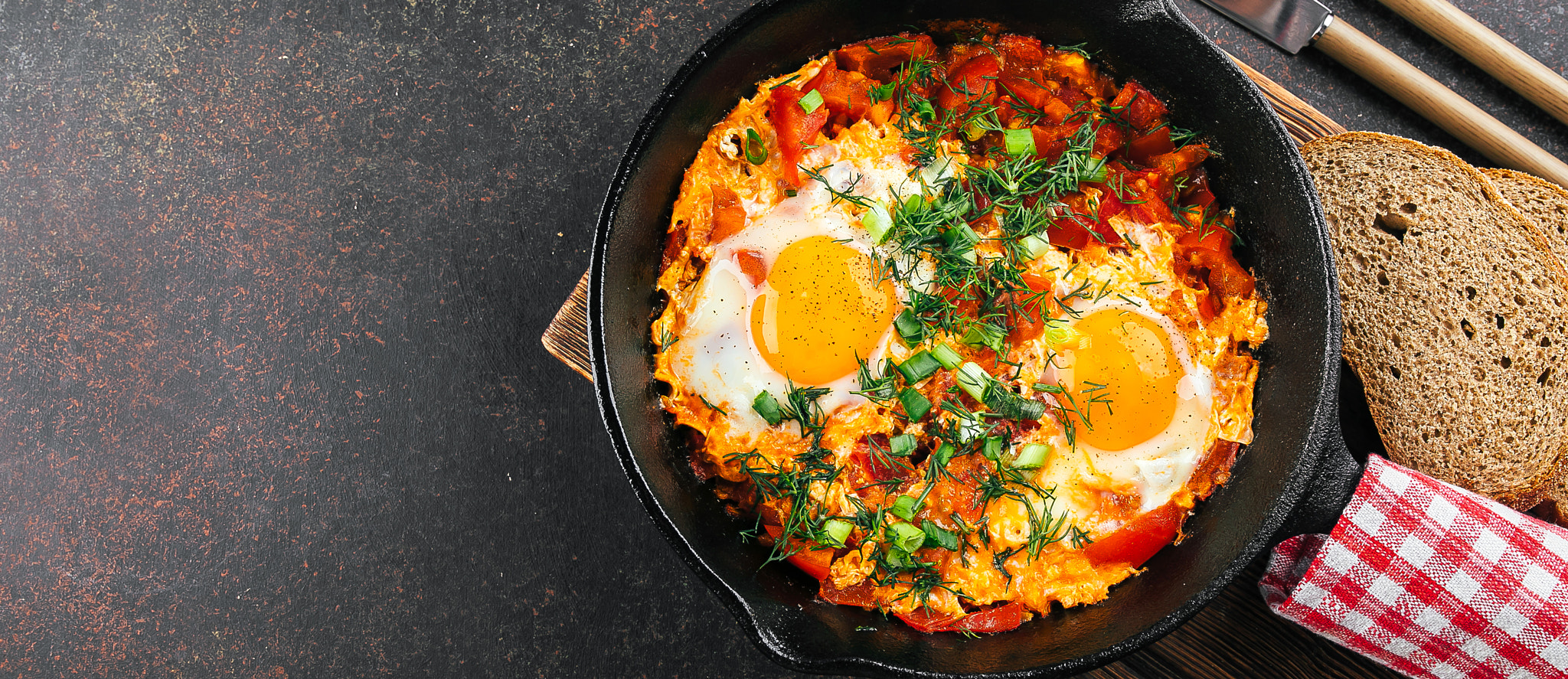 Shakshuka with eggs, tomato, and dill in iron pan. Top view, copy space. Banner image