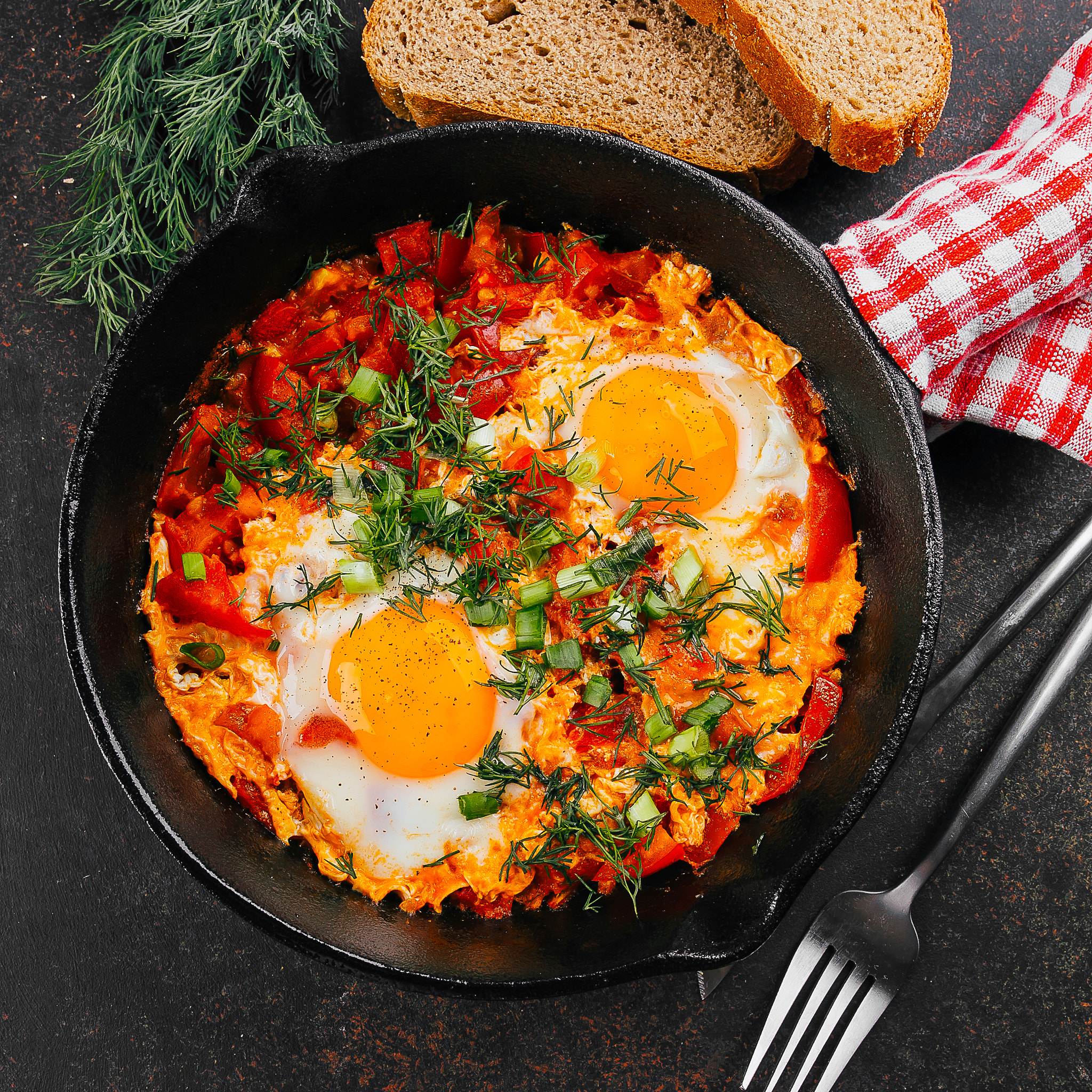 Top view of shakshuka with bread. Dish with eggs, tomato and dill in iron pan. Keto food diet