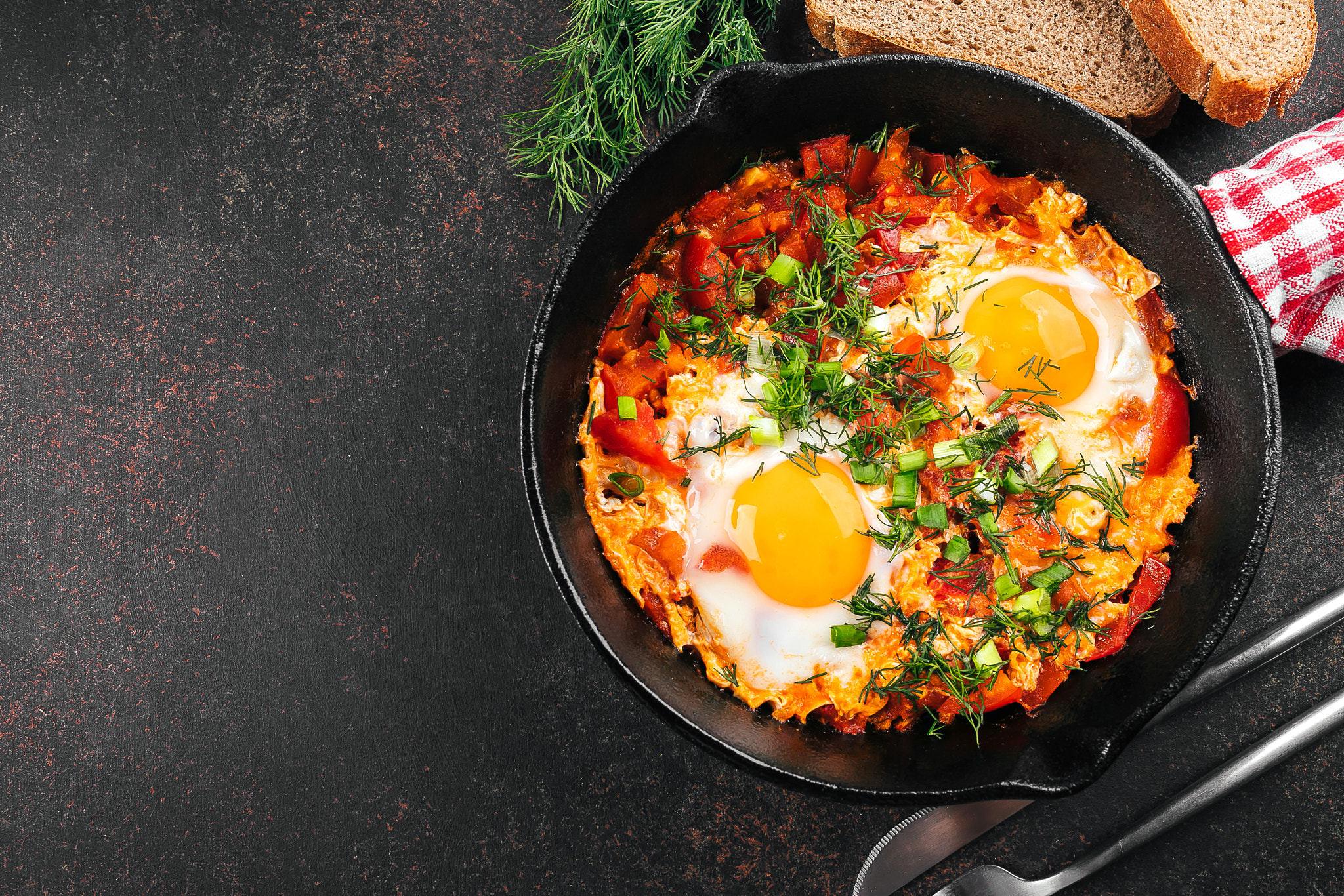 Breakfast food concept. Shakshuka with eggs, tomato, and dill in iron pan. Top view, copy space