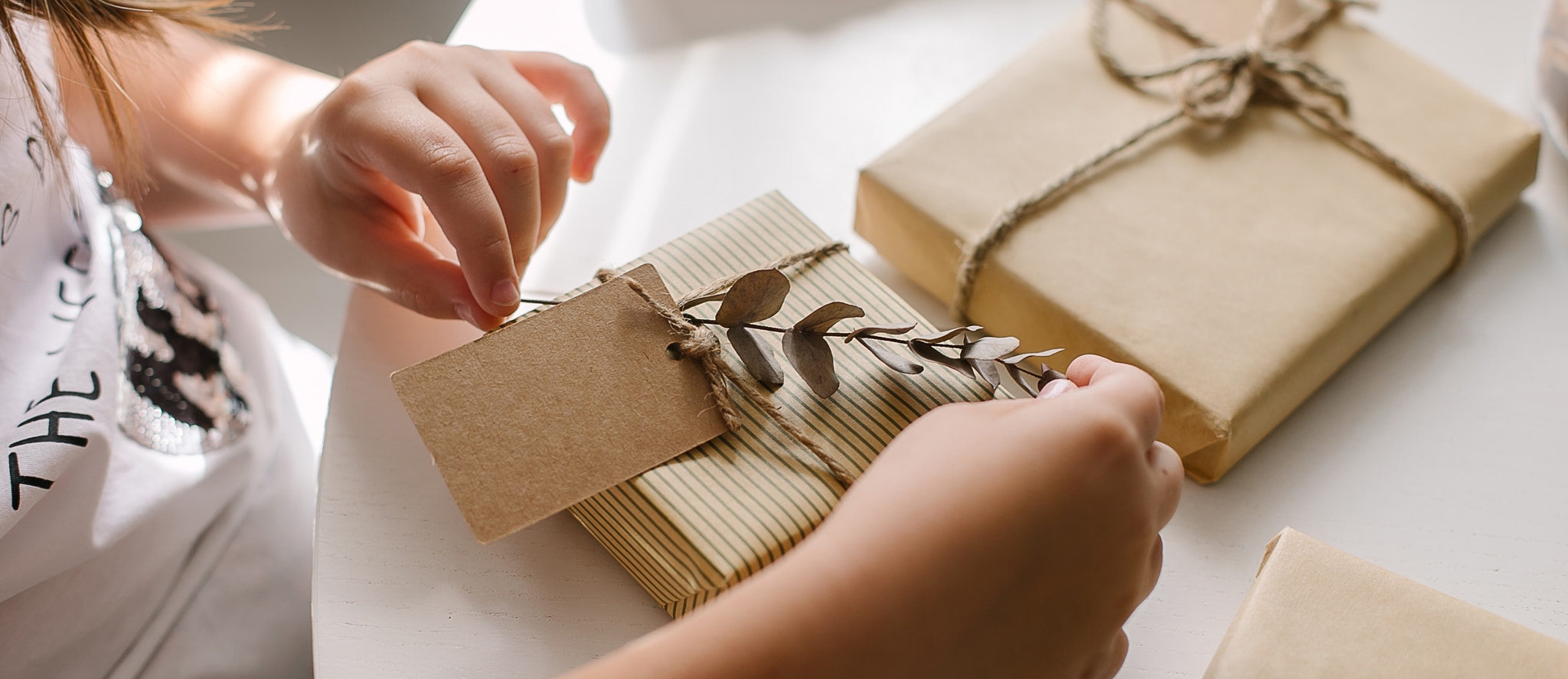 Female hands packing gift decor with eucalyptus and note cart for text. Zero waste Christmas