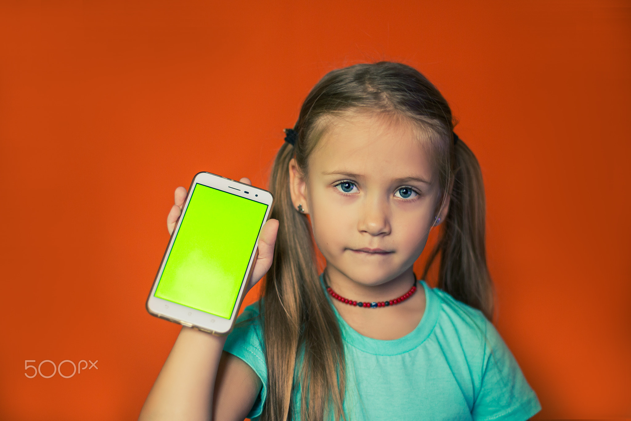 Child vertically holding smartphone with green screen.