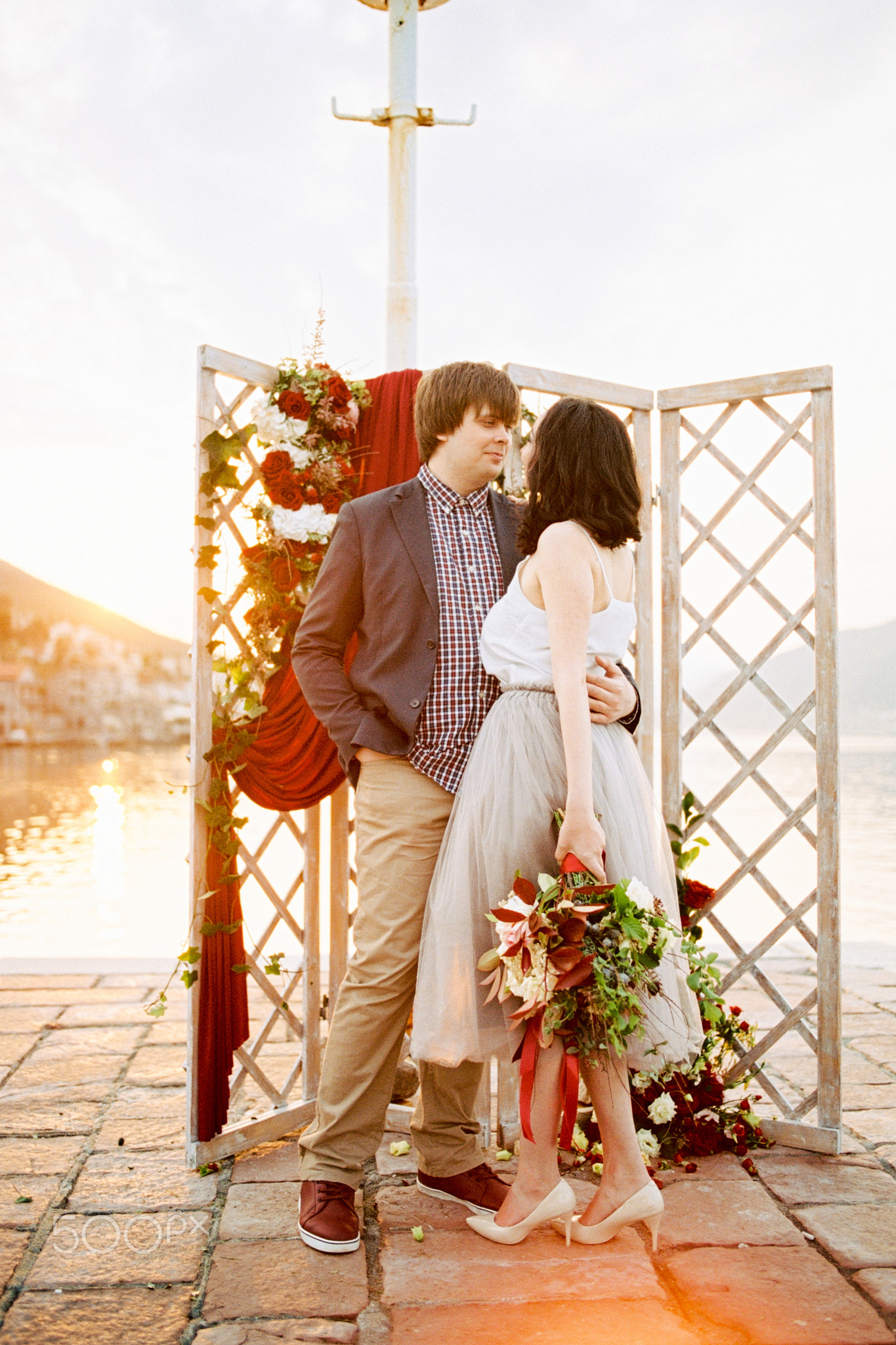 Groom hugs bride with a bouquet of flowers near the wedding screen on