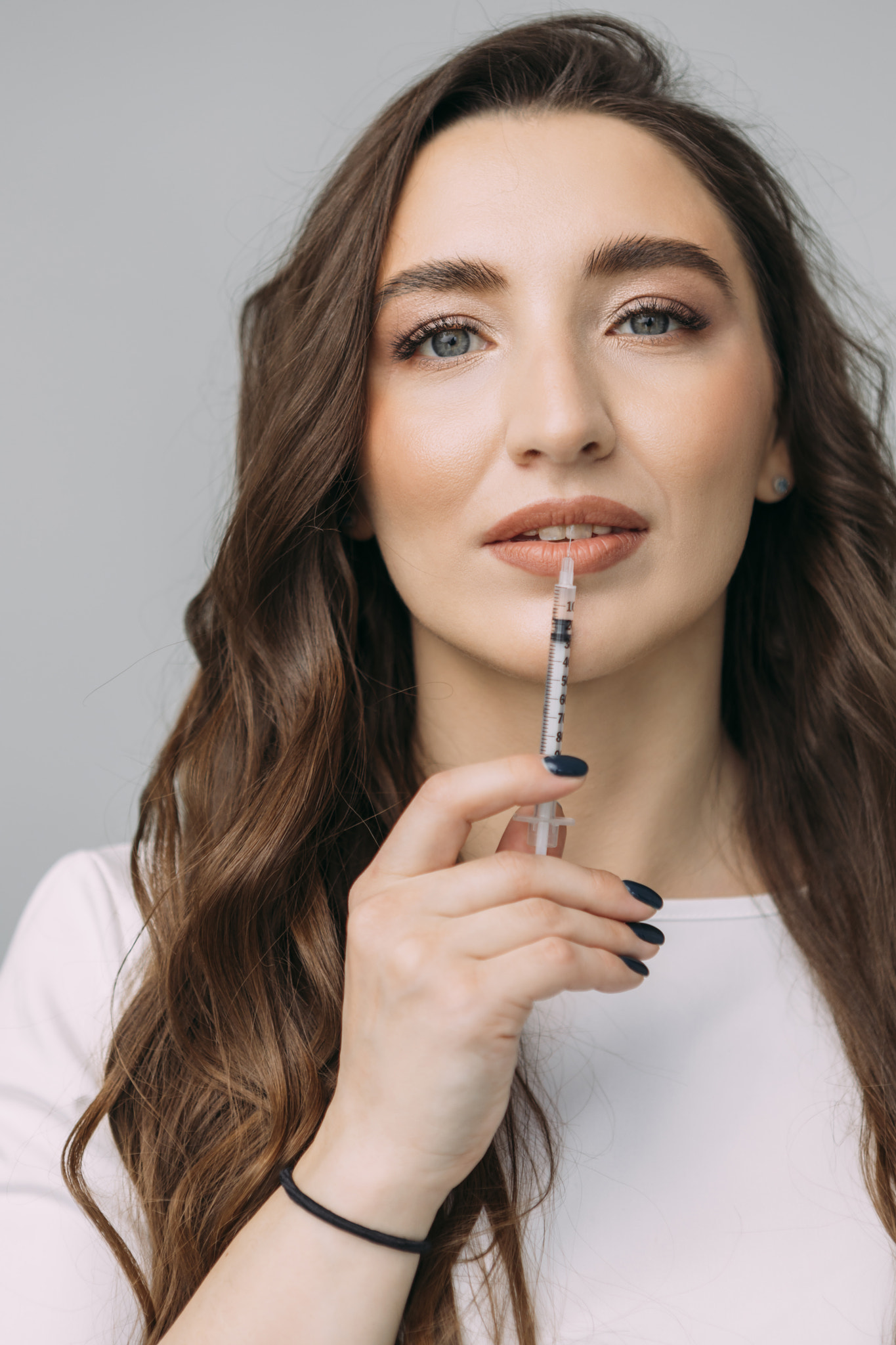 young girl doctor in a white coat on gray background makes herself an injection of hyaluronic acid t
