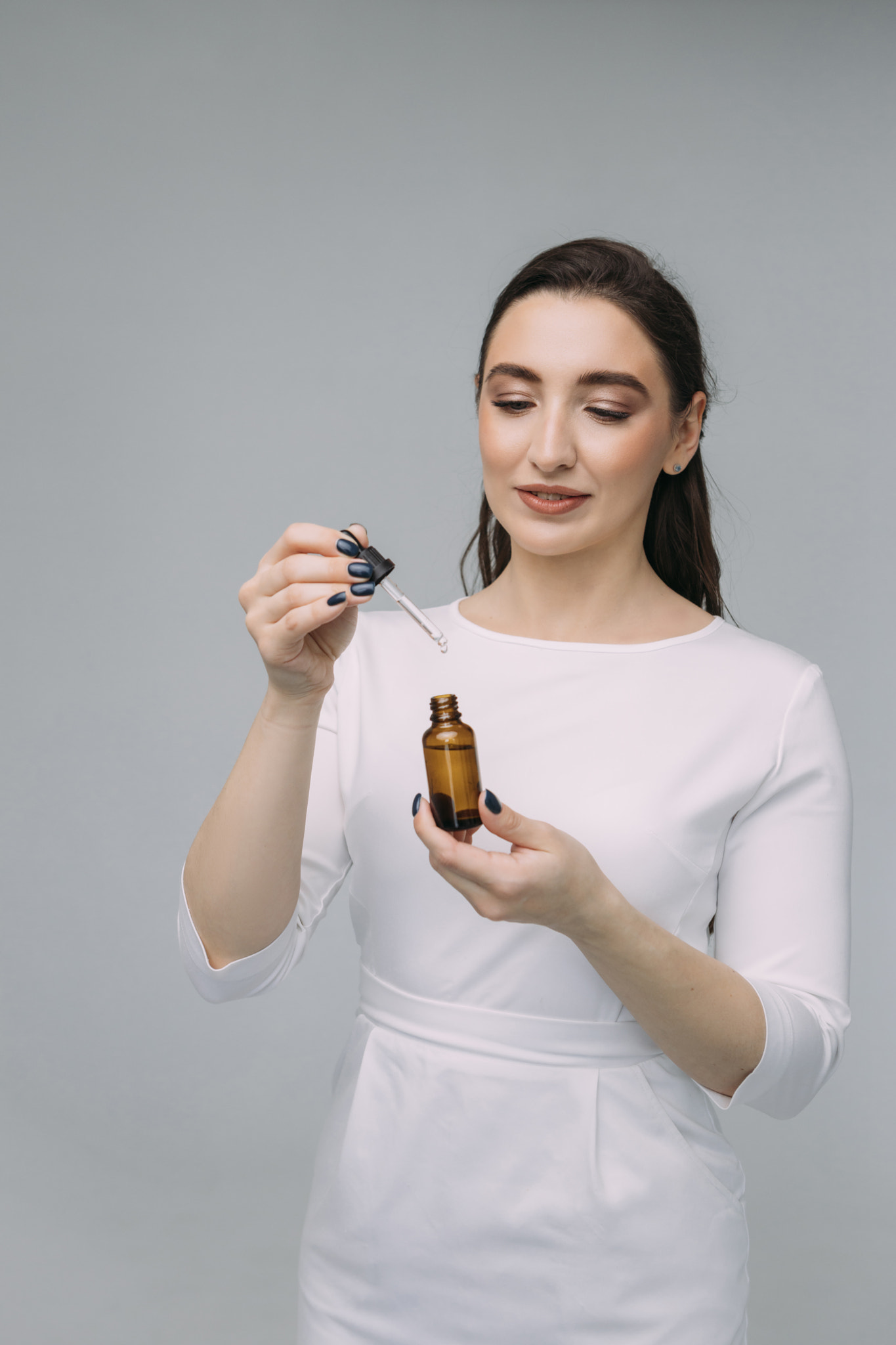 young girl doctor in a white coat-dress holds a pipette and a glass bottle with serum in her hands