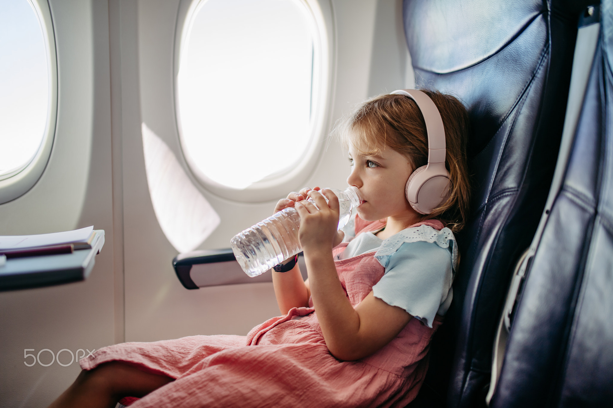 Little girl in airplane drinking water and listening music.