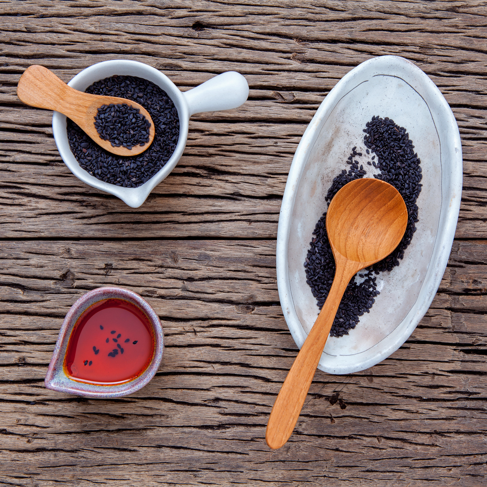 Black sesame oil and sesame seeds in white bowl set up on grunge wooden background.