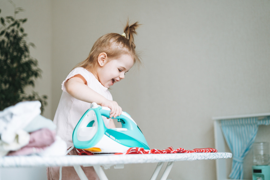 Jolie petite fille jouant et repassant des vêtements avec un fer à repasser à la maison par Galina Zhigalova sur 500px.com