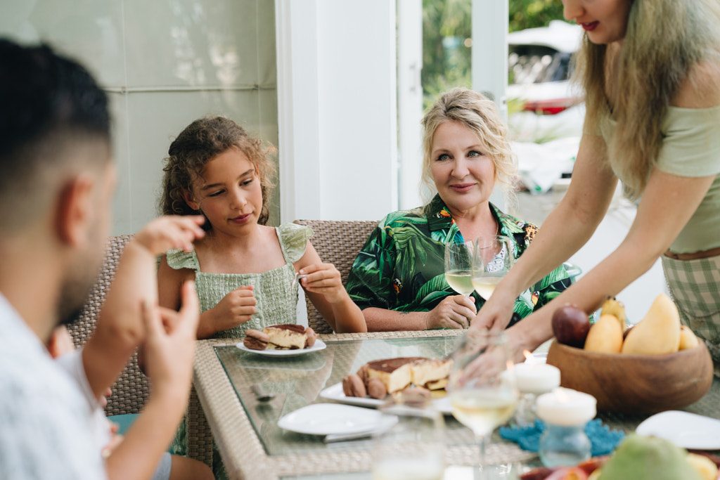 Young woman serving food to family at dining table by Natalie Zotova on 500px.com