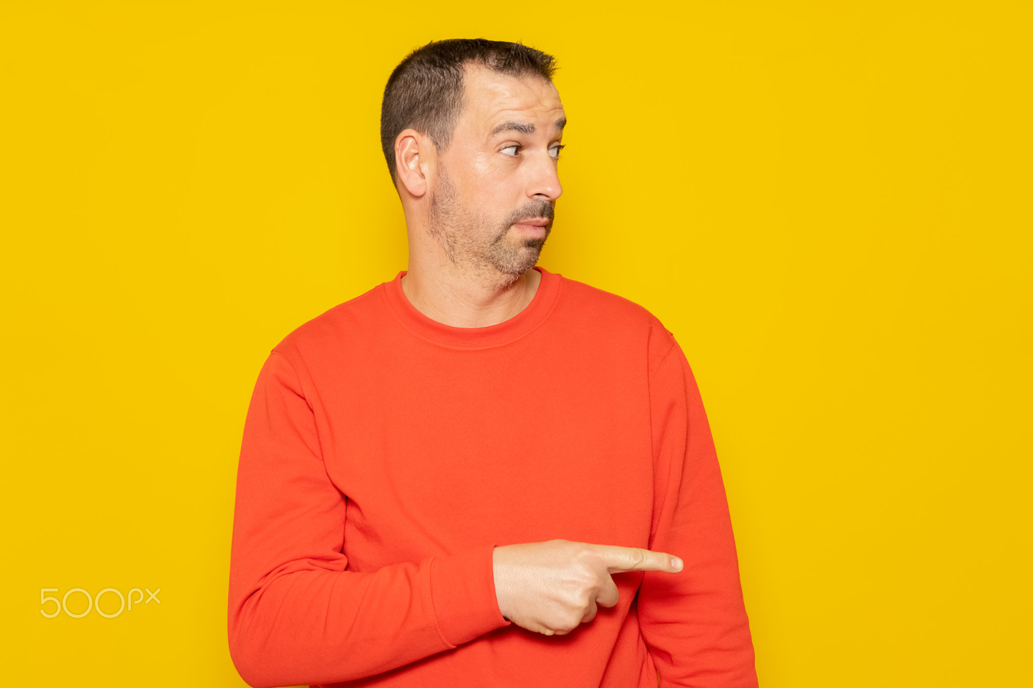 Bearded hispanic man wearing a red sweater pointing to the side with