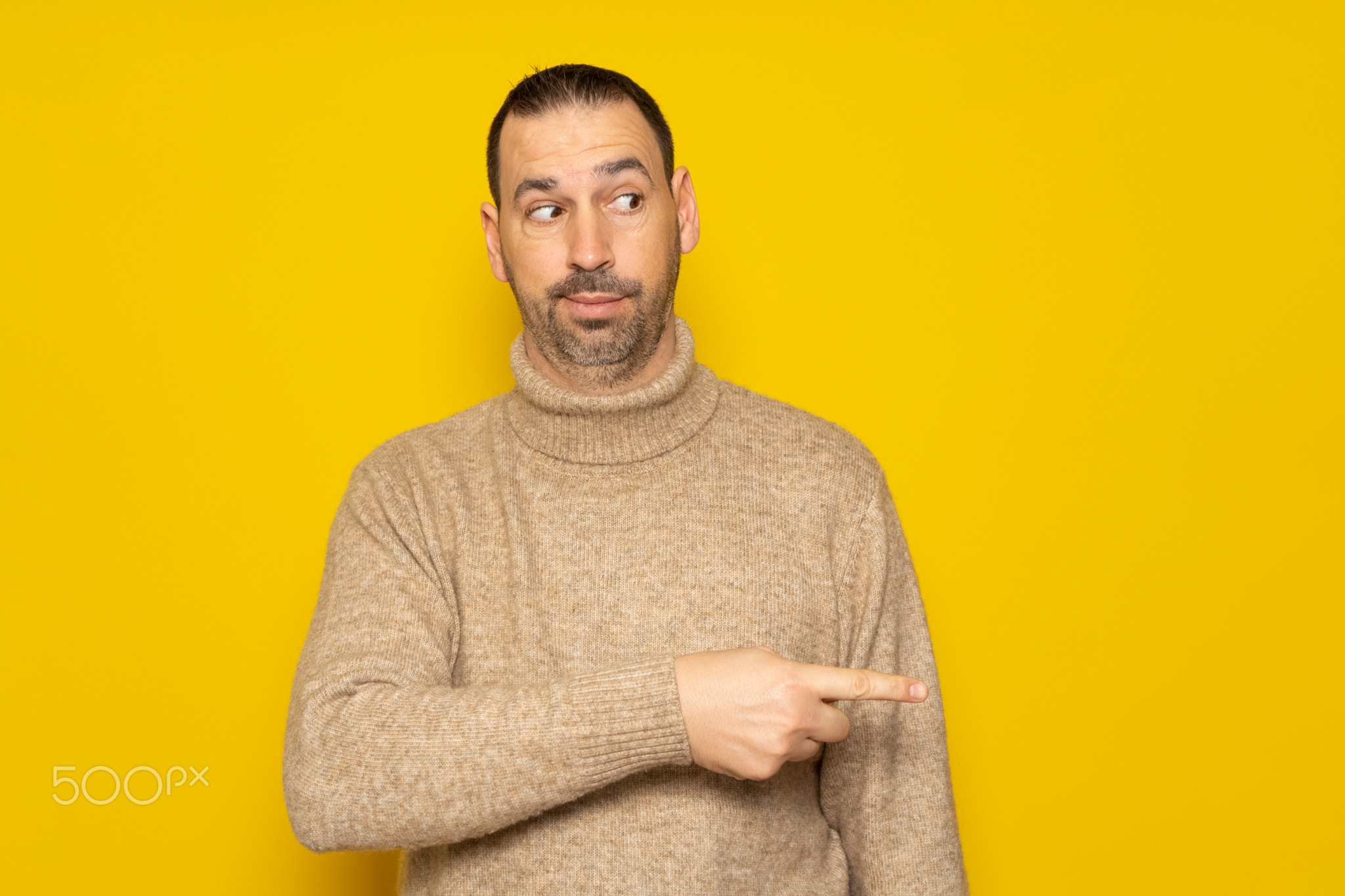 Hispanic man with a beard in a beige turtleneck pointing to the side