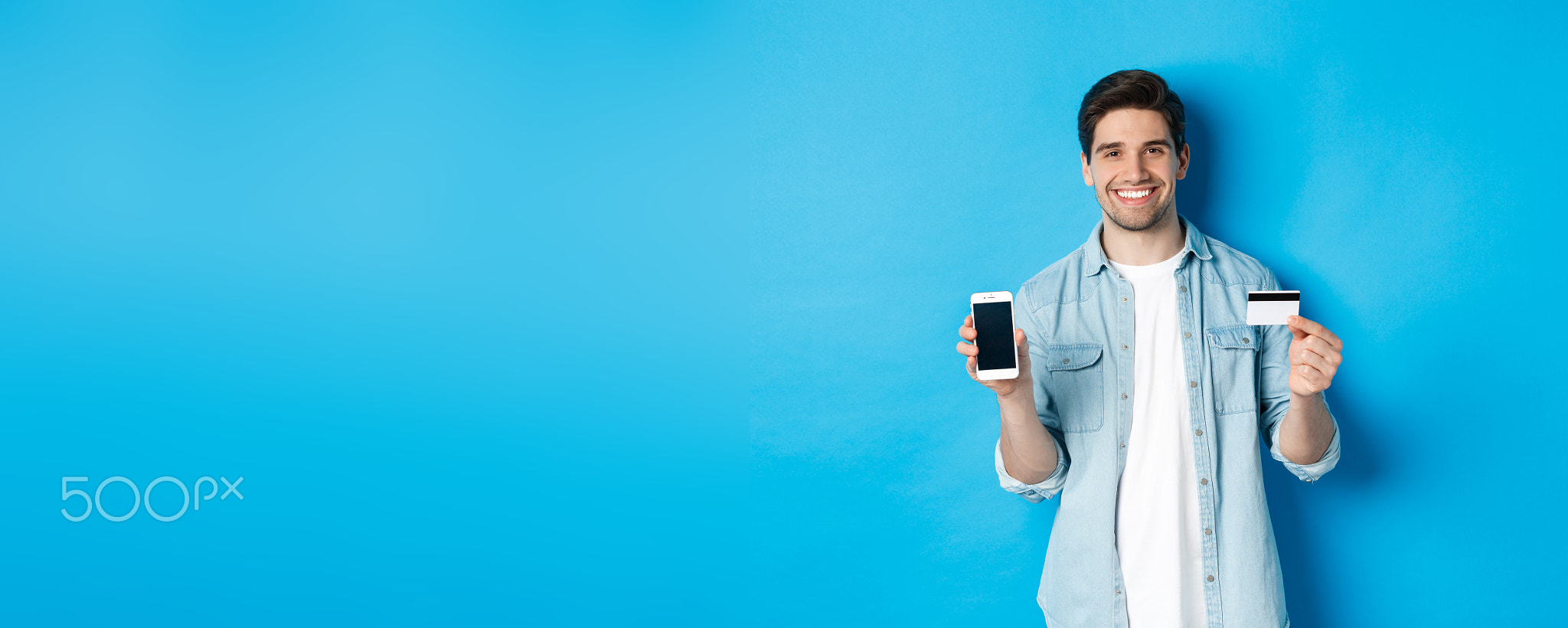 Young smiling man showing smartphone screen and credit card, concept