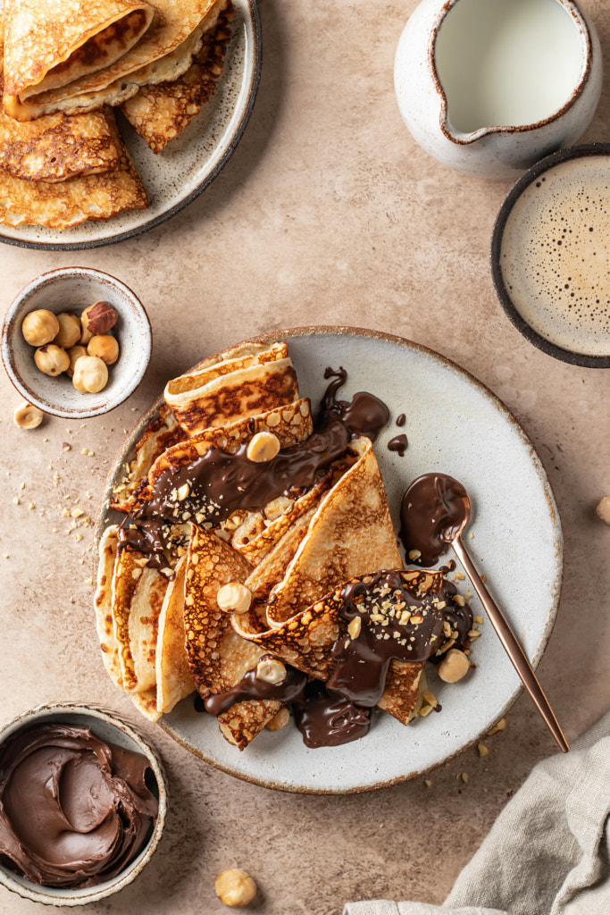 Crepes with chocolate and hazelnuts on beige background. Thin pancakes