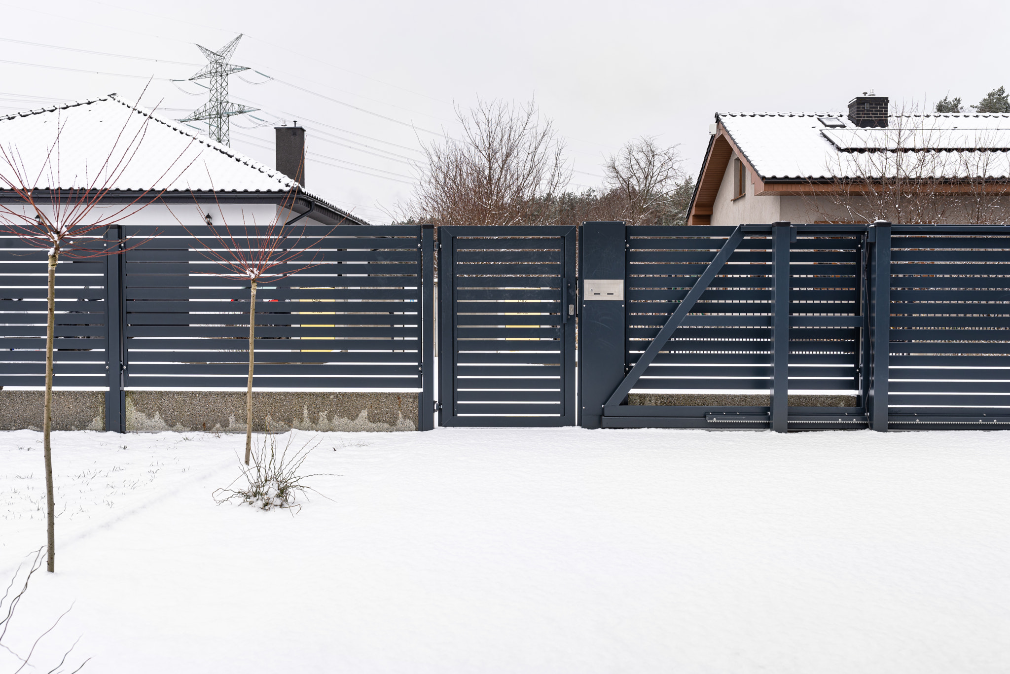 Modern panel fence in anthracite color, visible sliding gate and wicket with letterbox in winter.