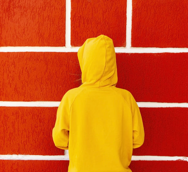 Teen girl in yellow sweatshirt from the back against background of red wall with white seams by Elena on 500px.com