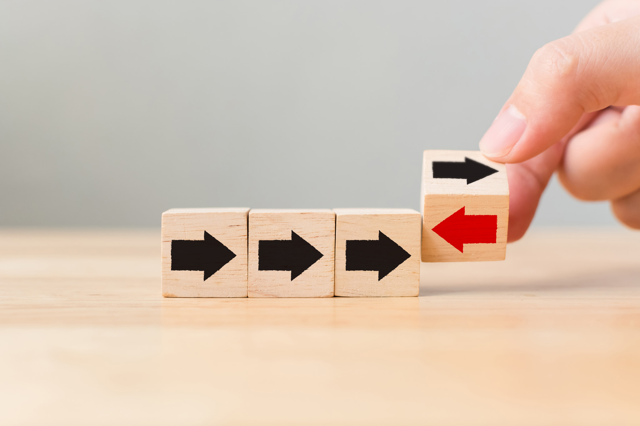 Hand flip over wooden cube block with red arrow facing the opposite direction black arrows, Unique,