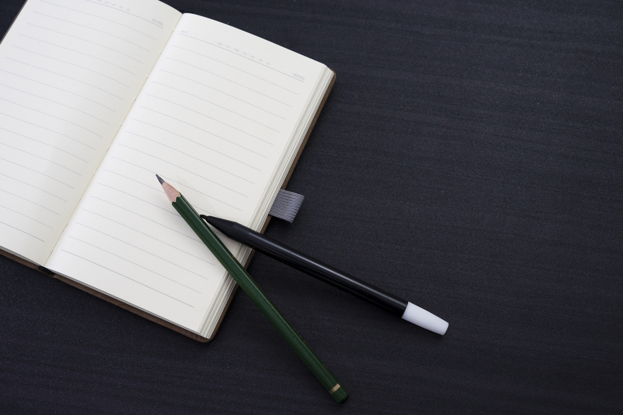 black desk with notebook and pencil on top of it a notebook