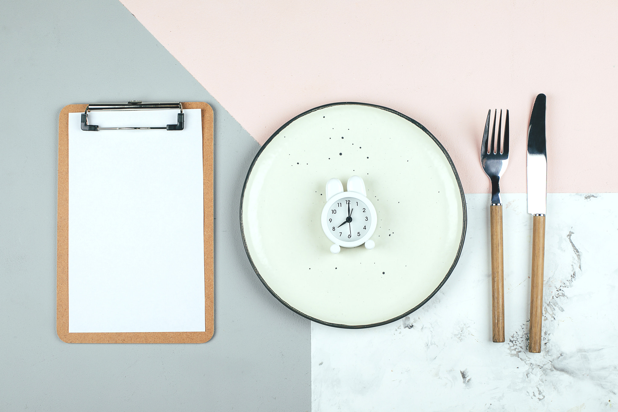 Intermittent fasting diet concept. Empty plate with alarm clock, note notepad. Flat lay, top view