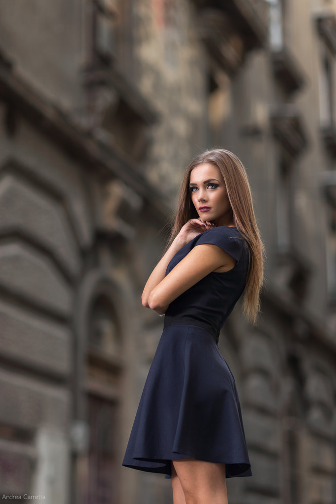 Portrait of beautiful young woman standing against buildings in city by ...