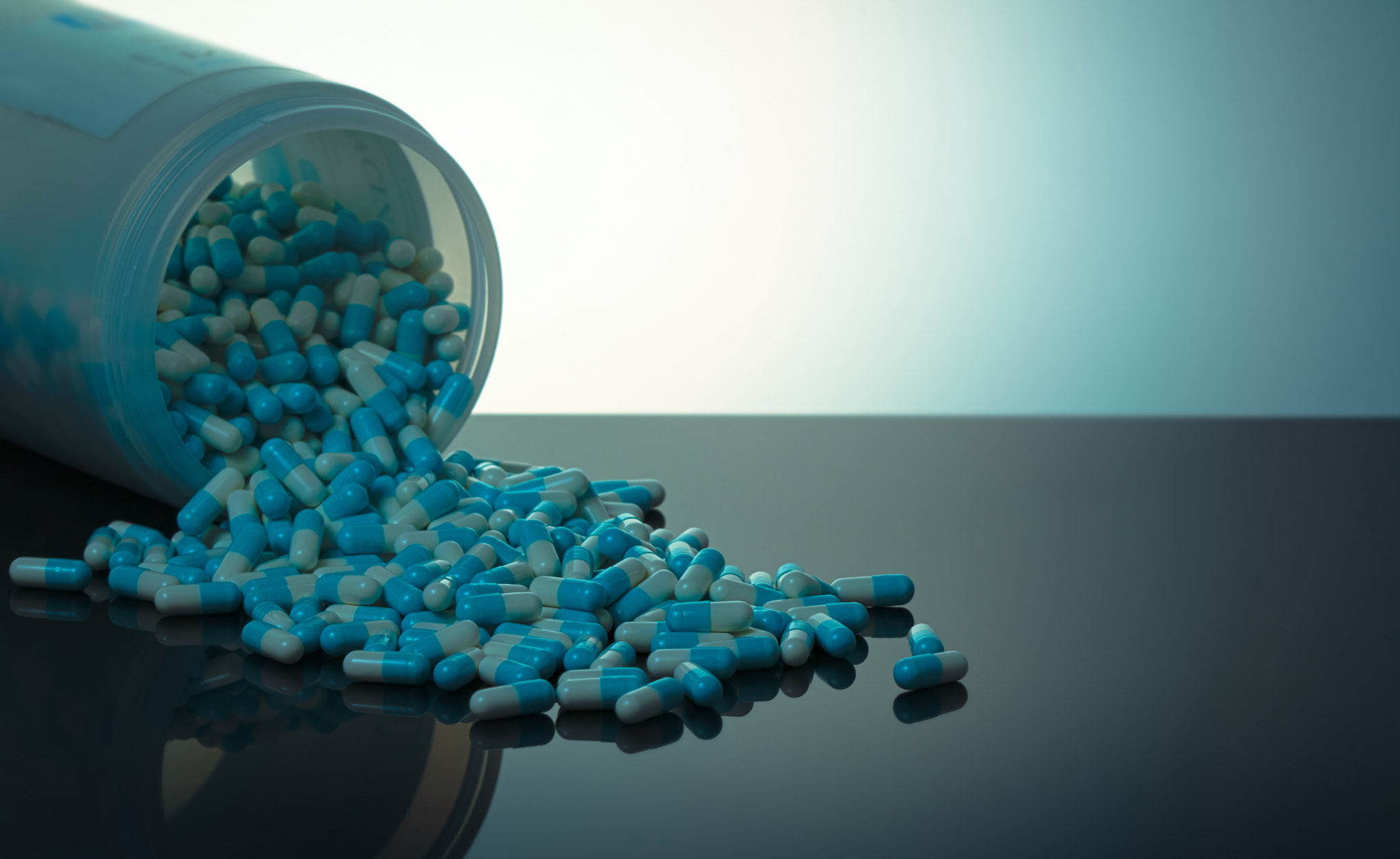 Blue and white capsule pill spilled out from white plastic bottle container. Global healthcare conce