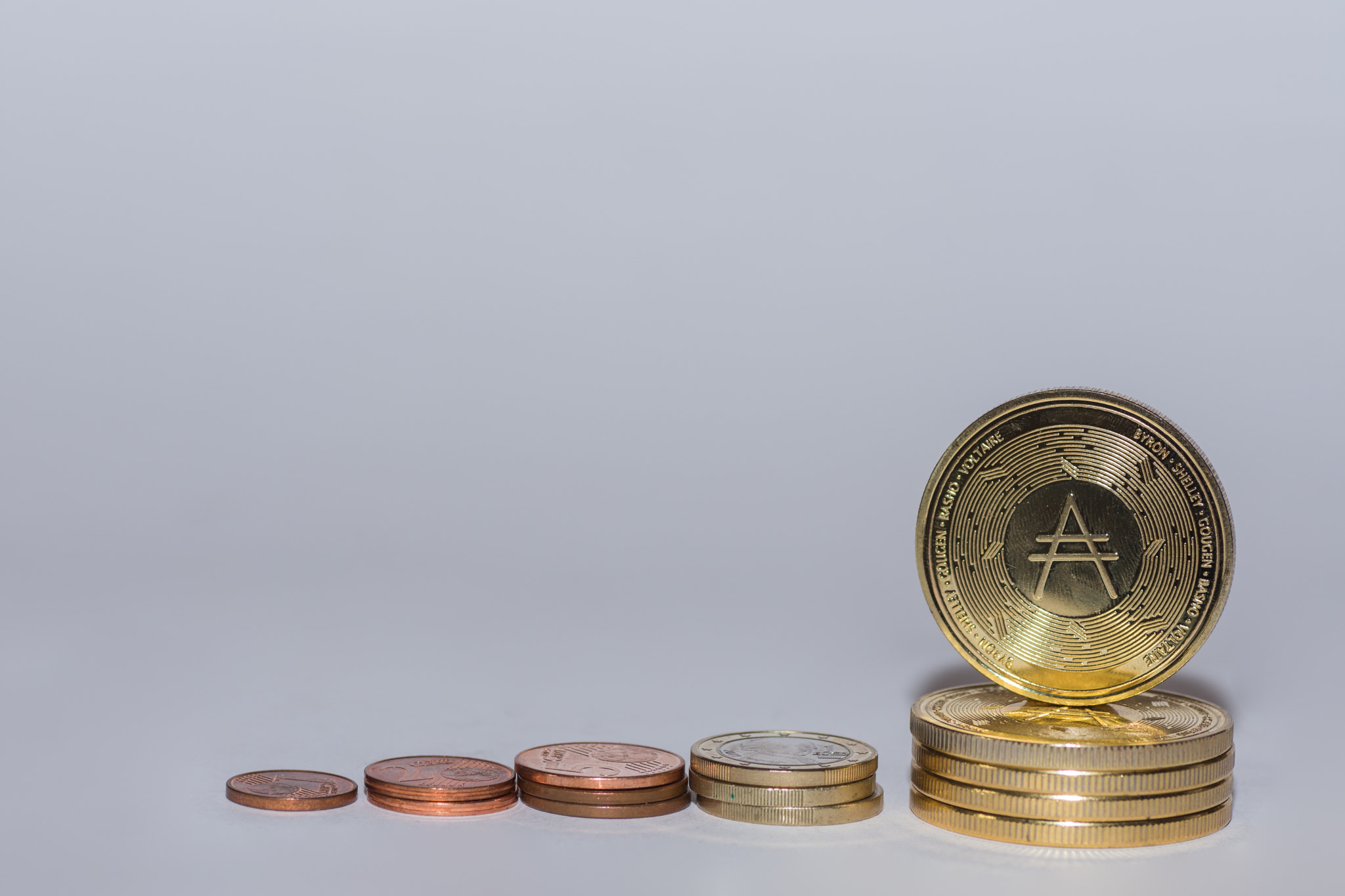 euro coins and ada coins from crypto currency stacked in a row with gray