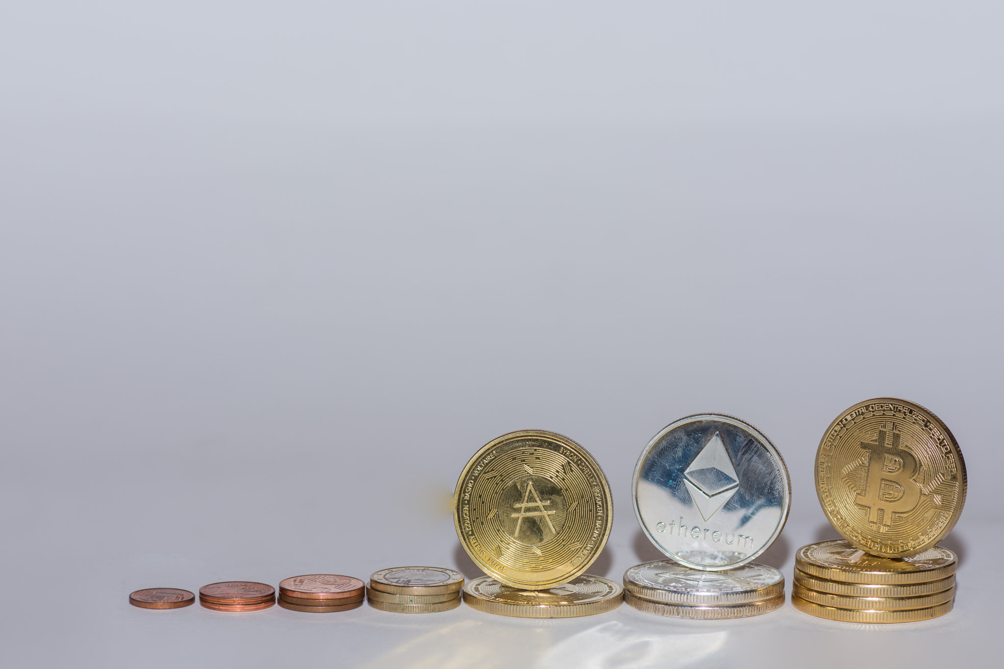 euro coins and crypto coins bitcoin ether and ada in a row with gray background oblique