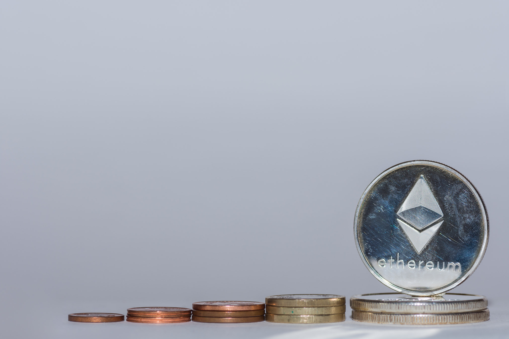 euro coins and silver ether coins from crypto currency stacked in a row with gray background flat