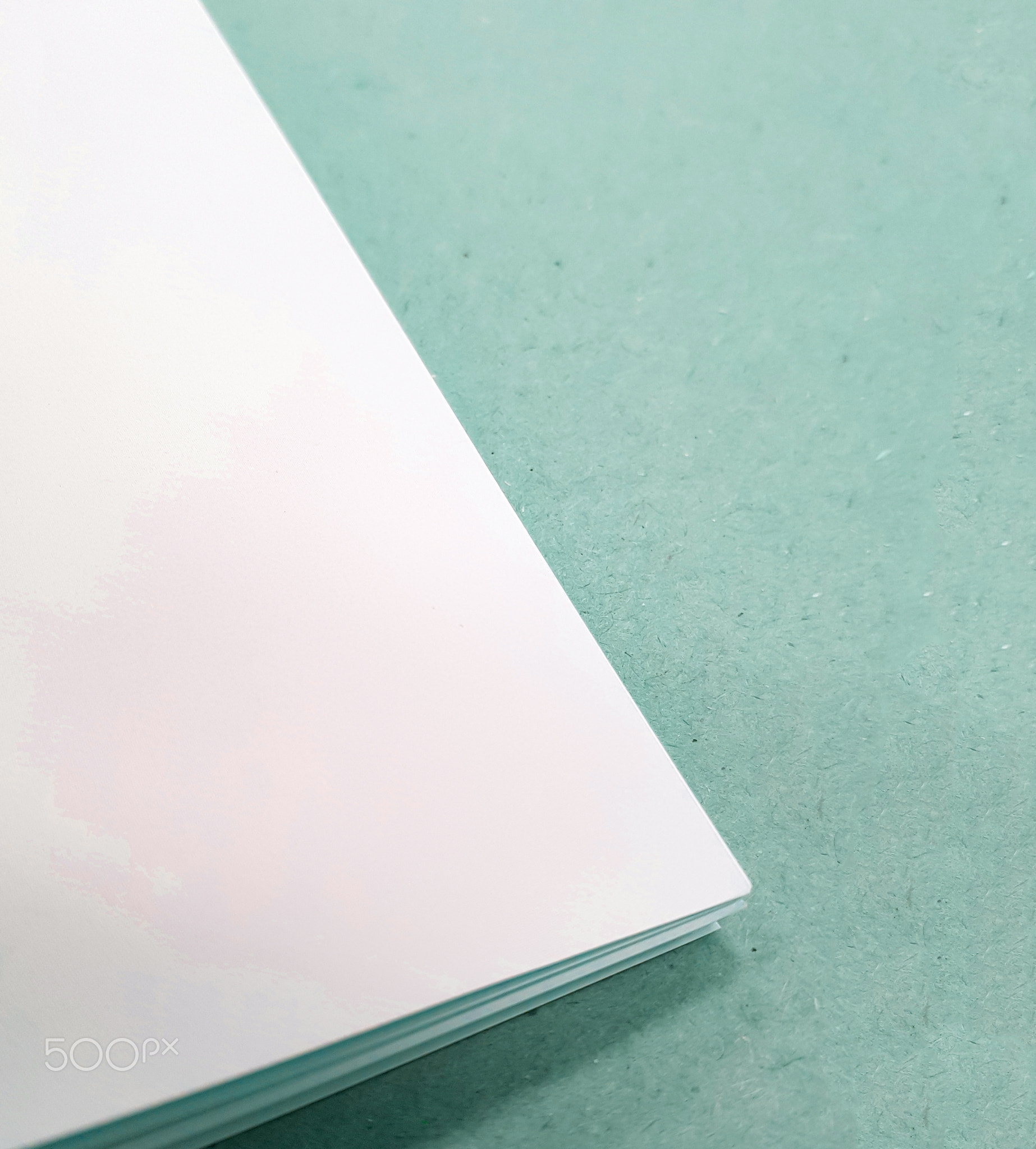 A corner of a stack of white paper sheets lies on a green background
