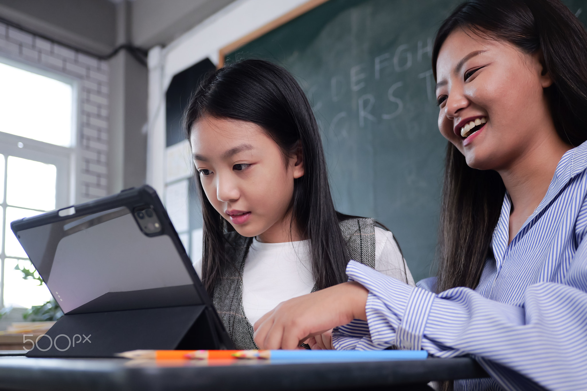 Happy student studying with teacher in classroom at school