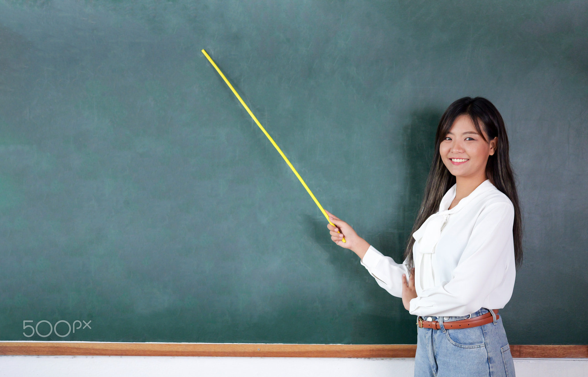 Teacher standing near backboard holding textbook posing to camera with