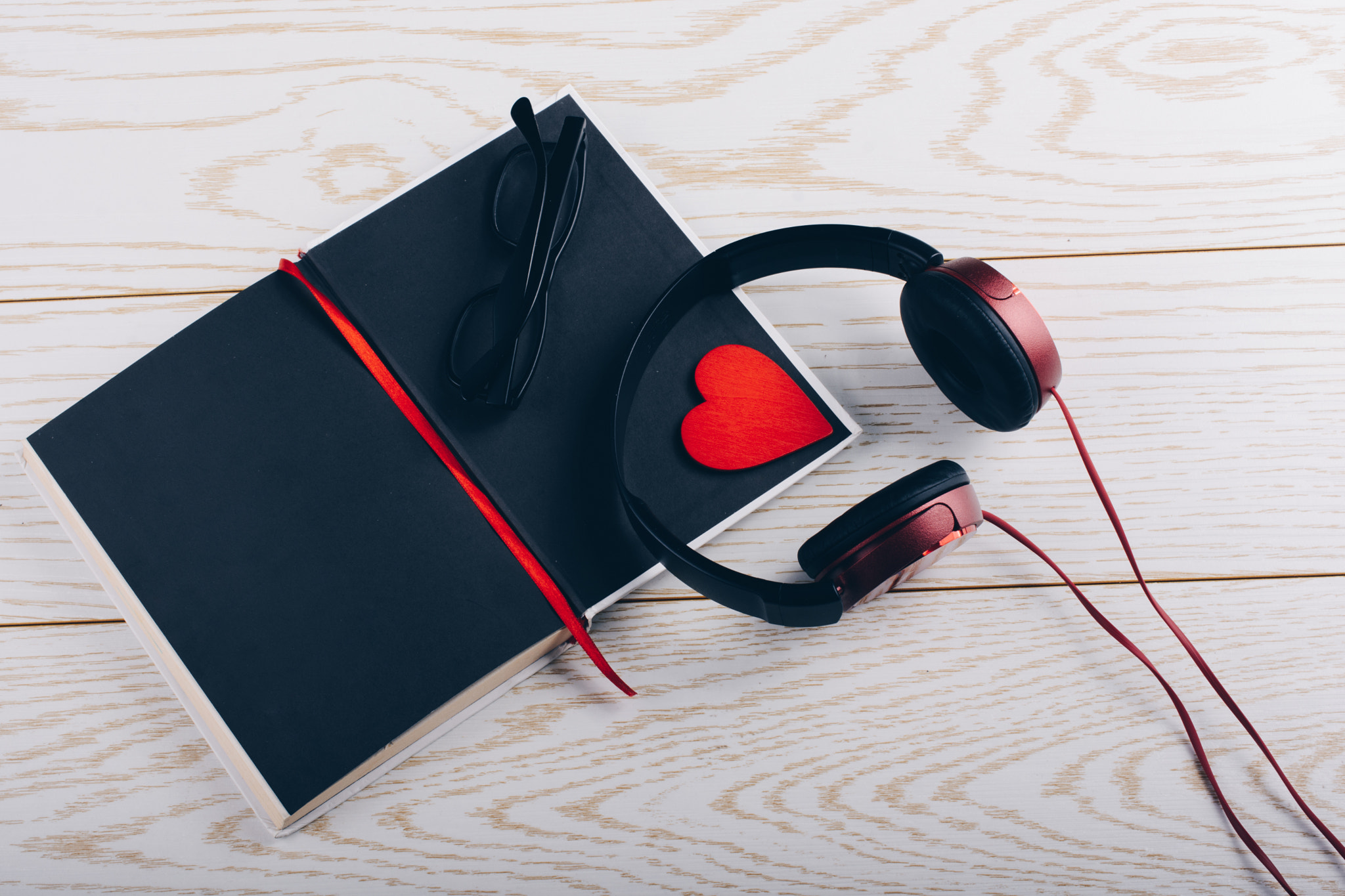 Headphones, notebook, pen, glasses and heart on wooden background