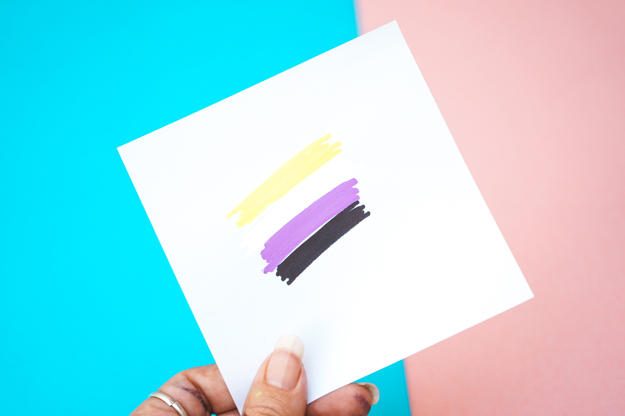 Hand holding a paper with non-binary flag drawing in it