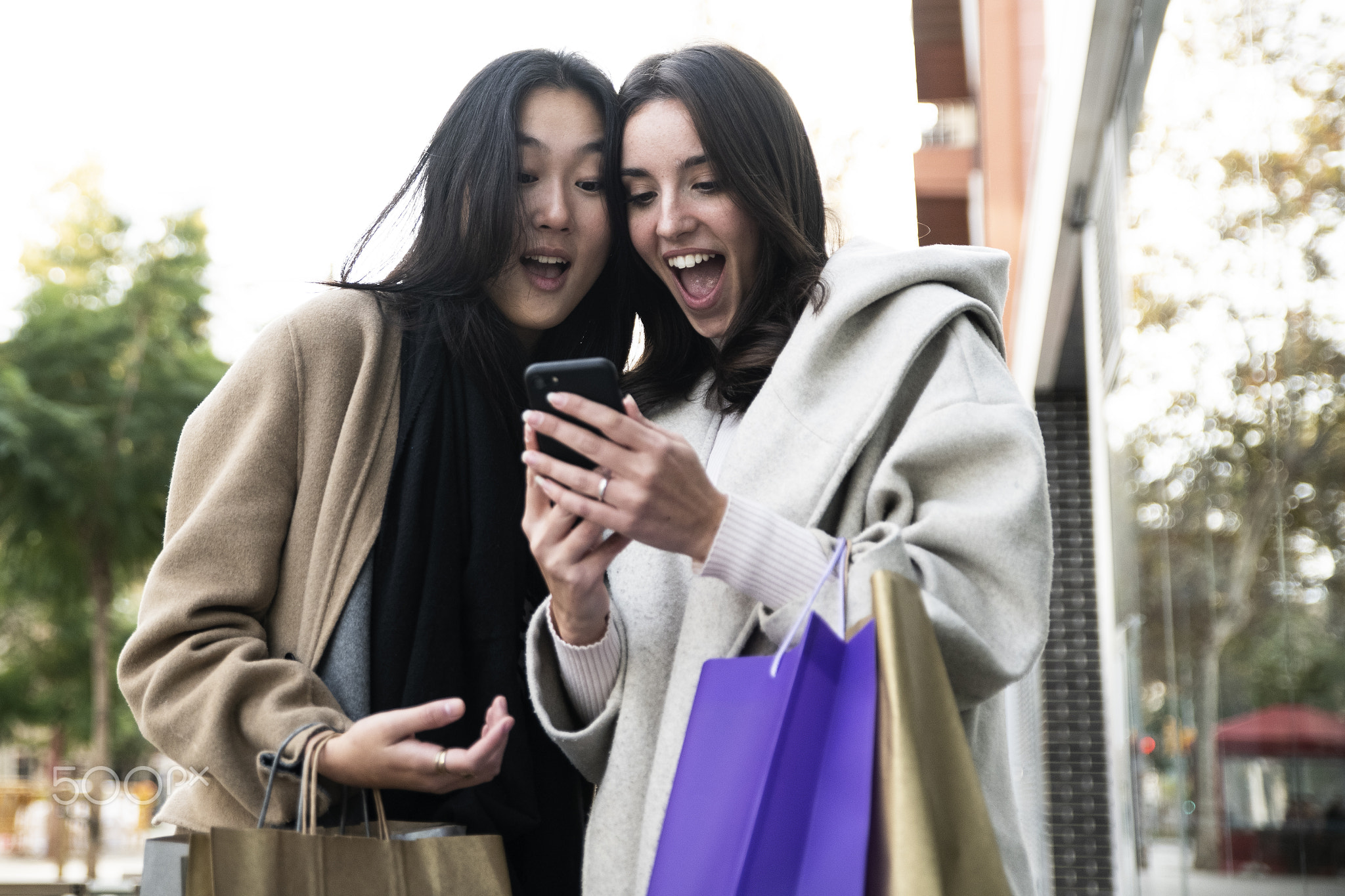 Two surprised young beautiful women holding shopping bags and looking