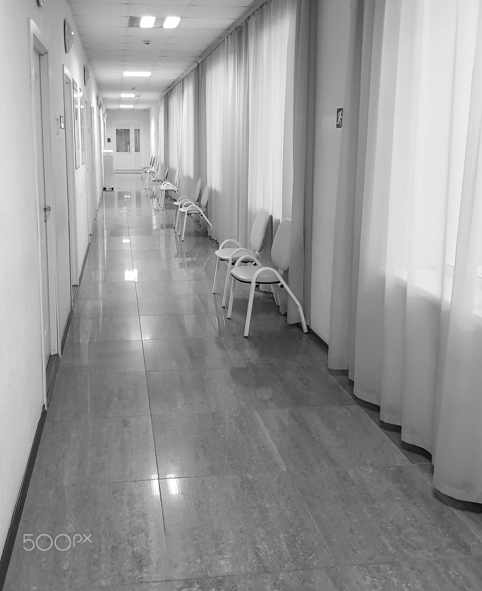 A long corridor with curtains on the windows and chairs in front of