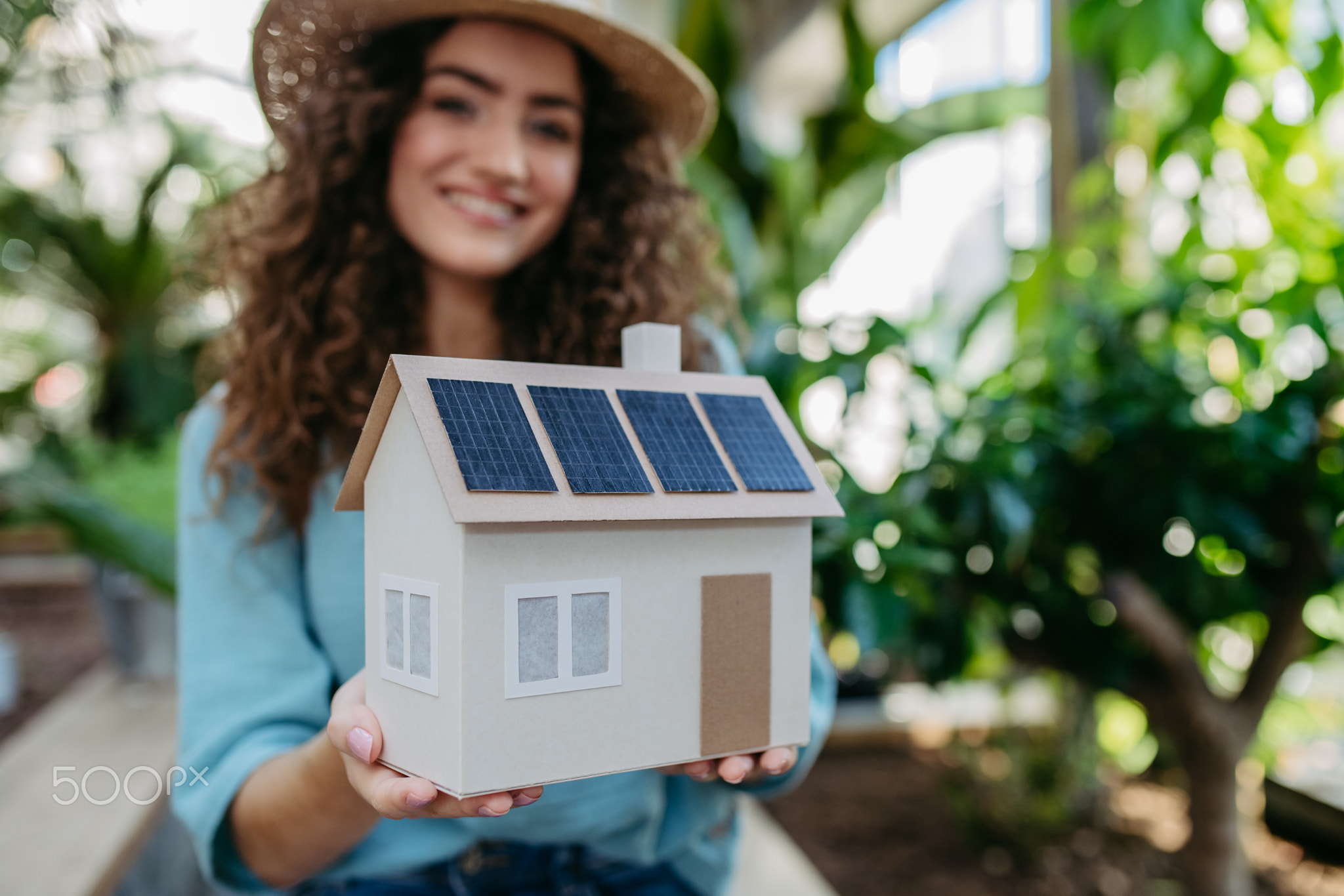 Young woman in botanical garden holding model of house with solar
