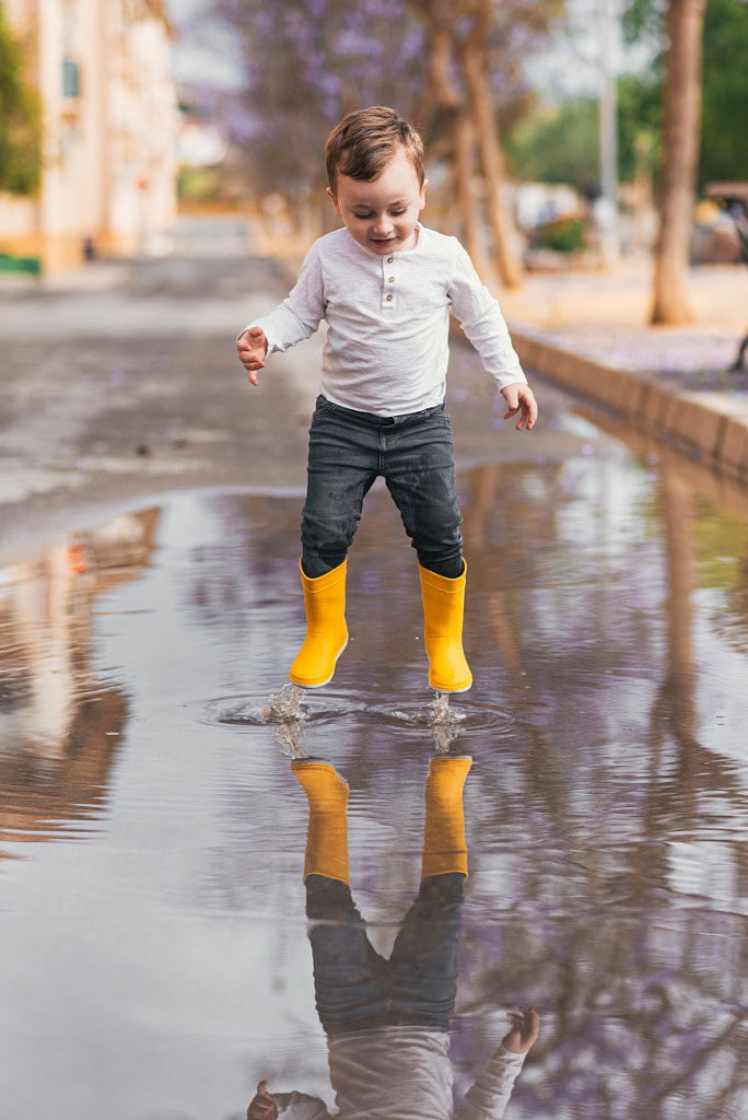 garçon en bottes de caoutchouc jaune sautant par-dessus une flaque d'eau sous la pluie par Miri Garcia sur 500px.com