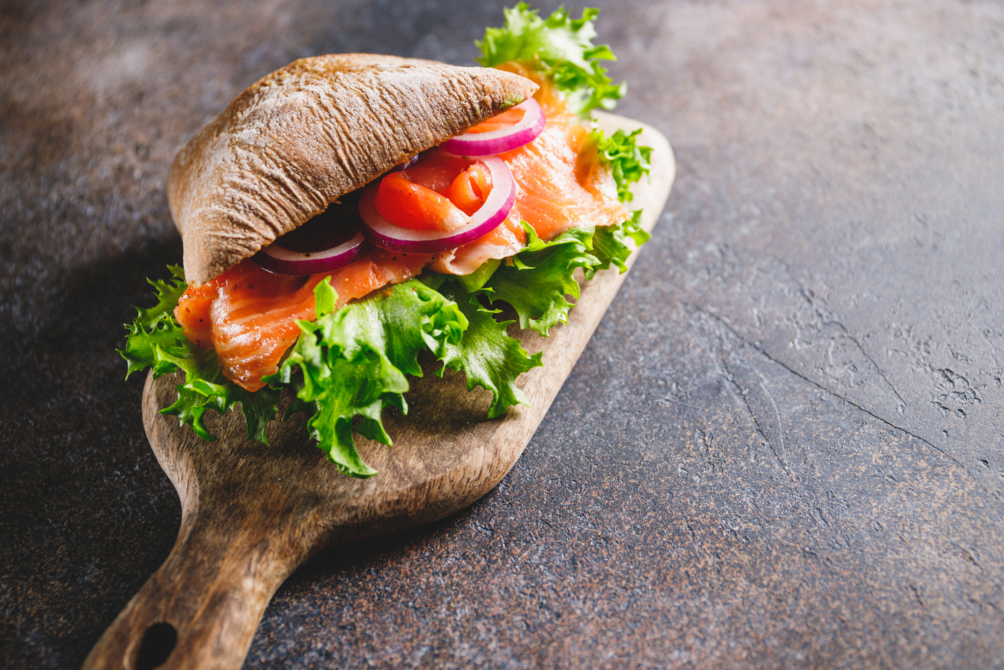 Healthy sandwich with rye bread bun, salmon, avocado, onion and salad served on a wooden rustic boar