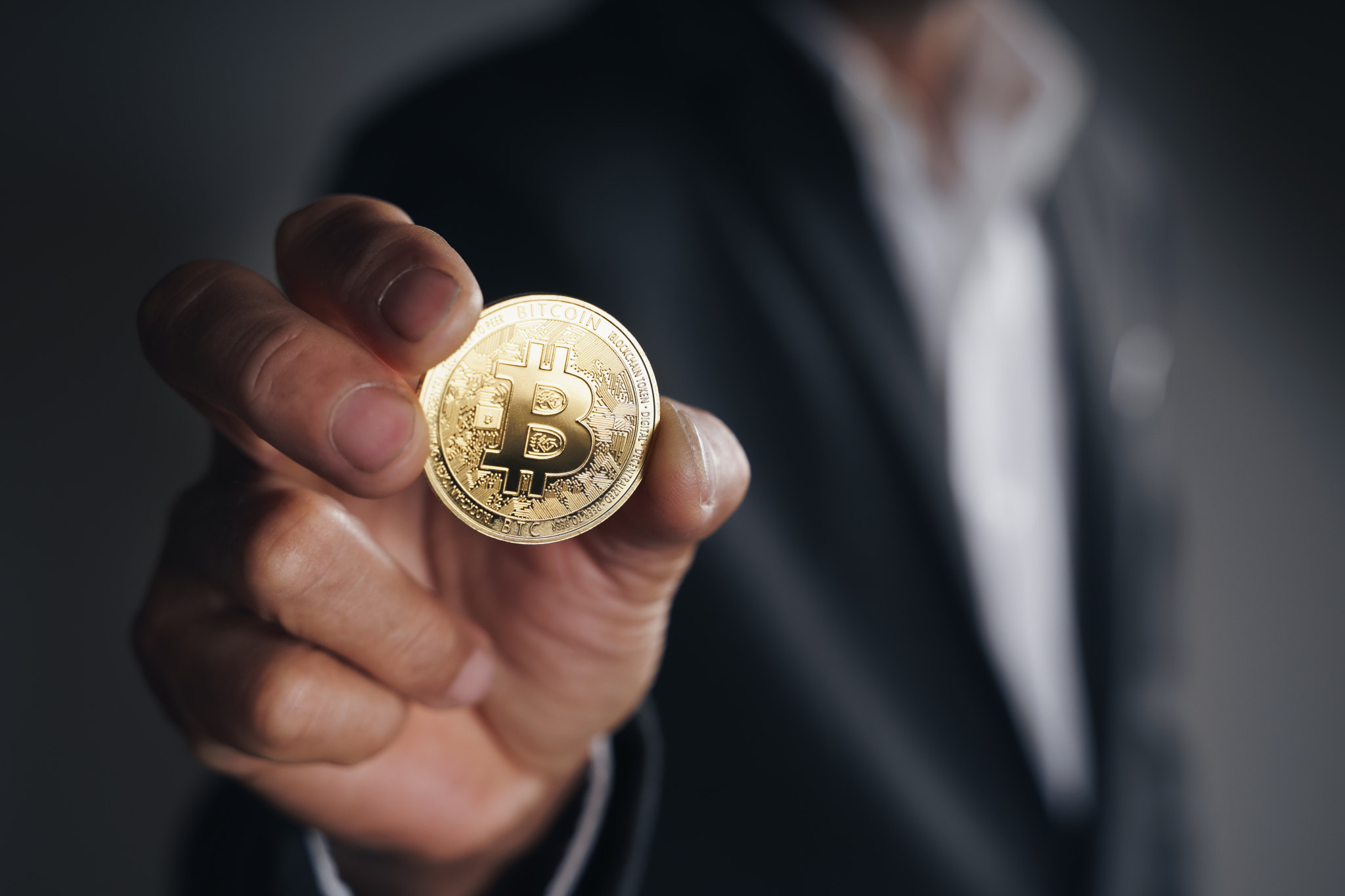 Handsome Investor Businessman in black suit holding a golden bitcoin on dark background, trading, Cr