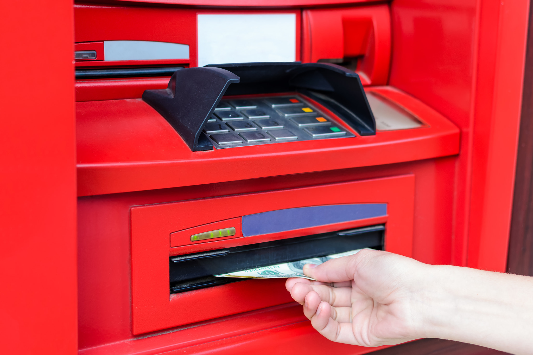 Woman's hand takes cash USD from red ATM
