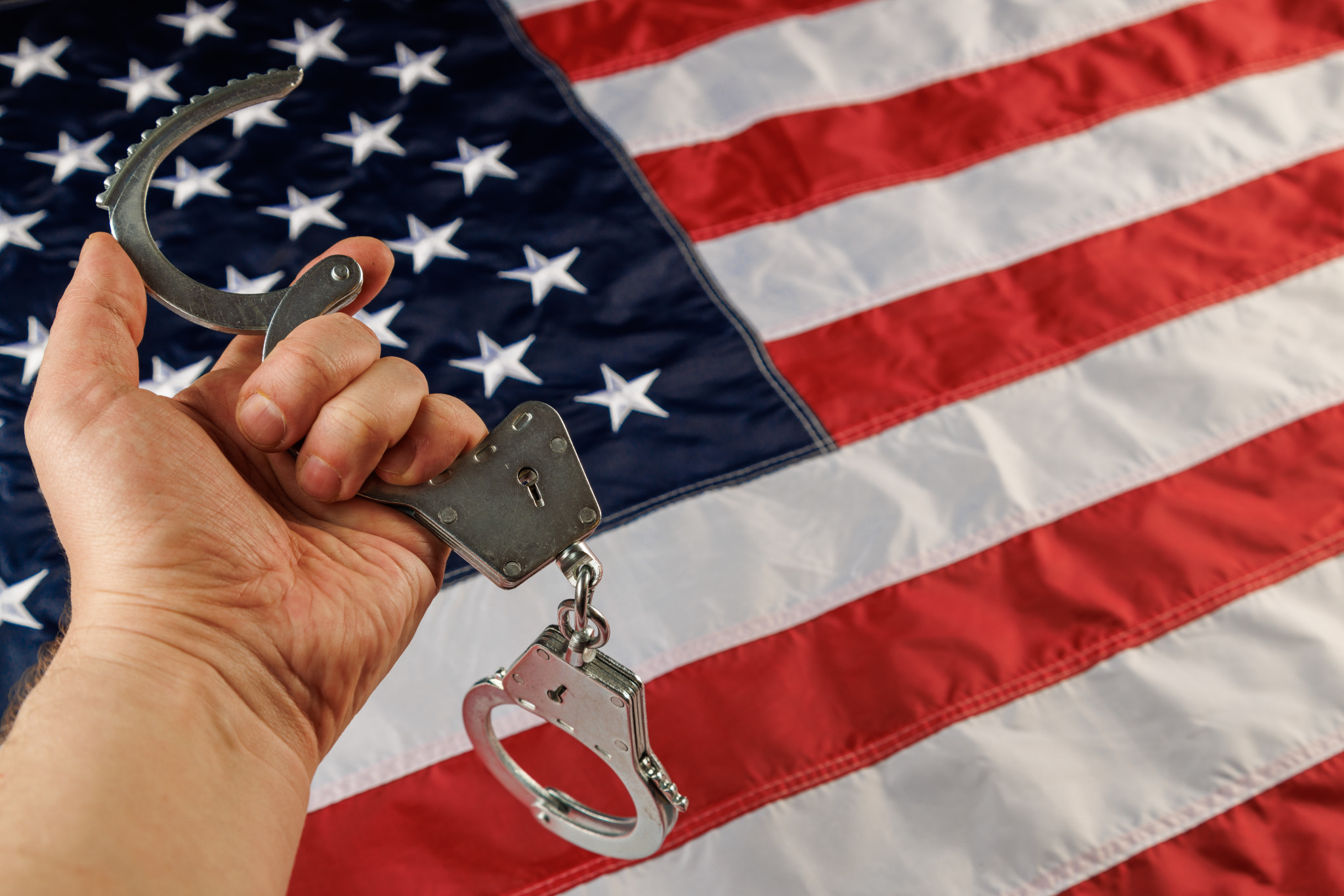 caucasian hand holding silver metal handcuffs over US flag background