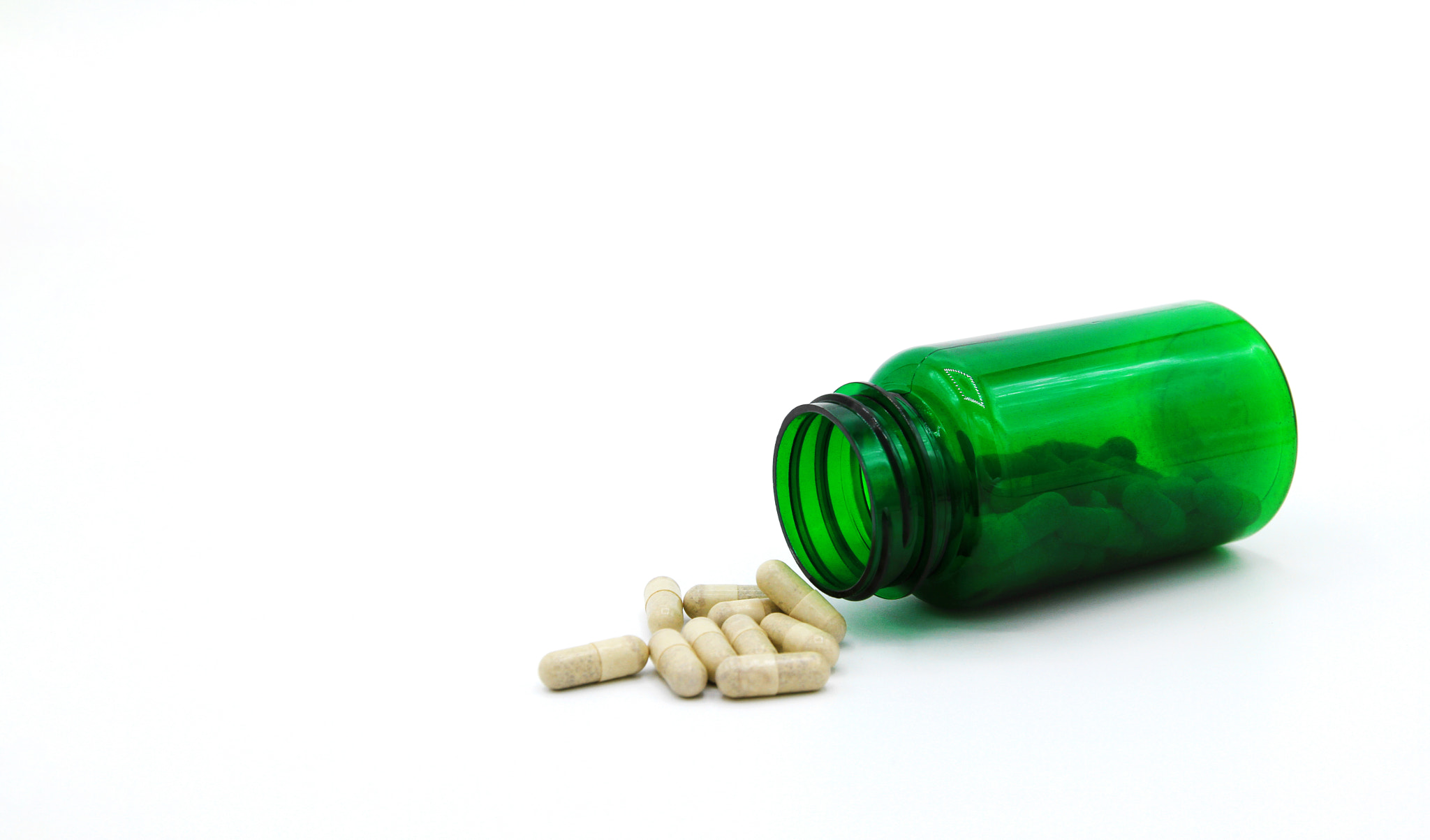 White pills spilling or pour out of green pill bottle isolated on white background with copy space