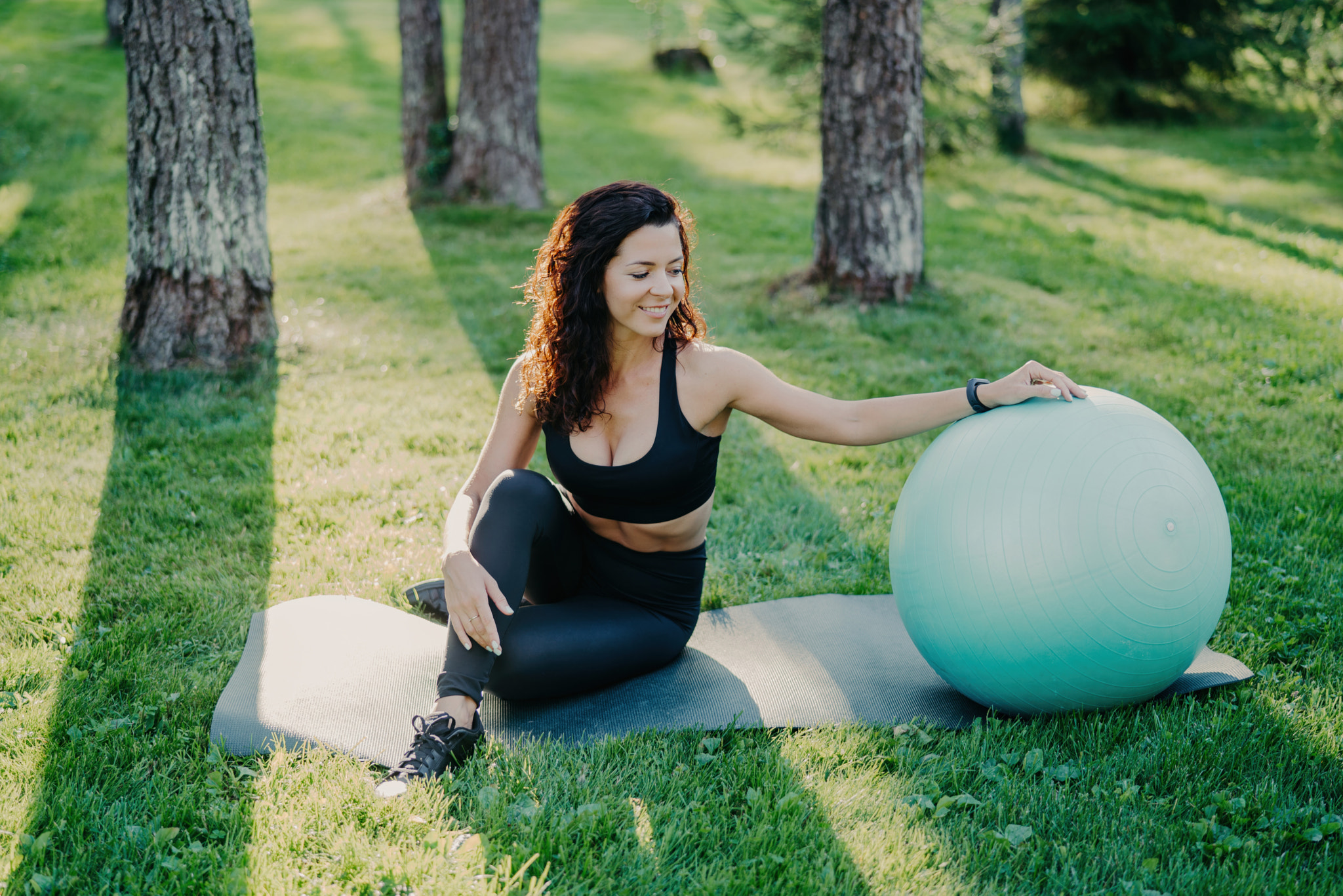 Outdoor shot of active sporty woman takes break after physical exercises, poses on fitness mat with