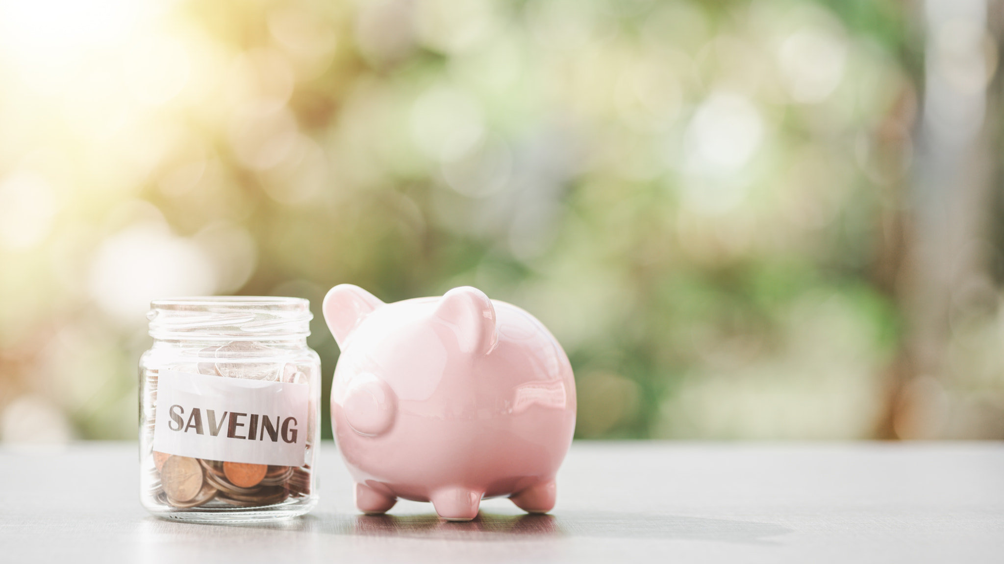 siveing text in a piece of paper and coins in a glass jar, pink piggy bank, all on the table, saving